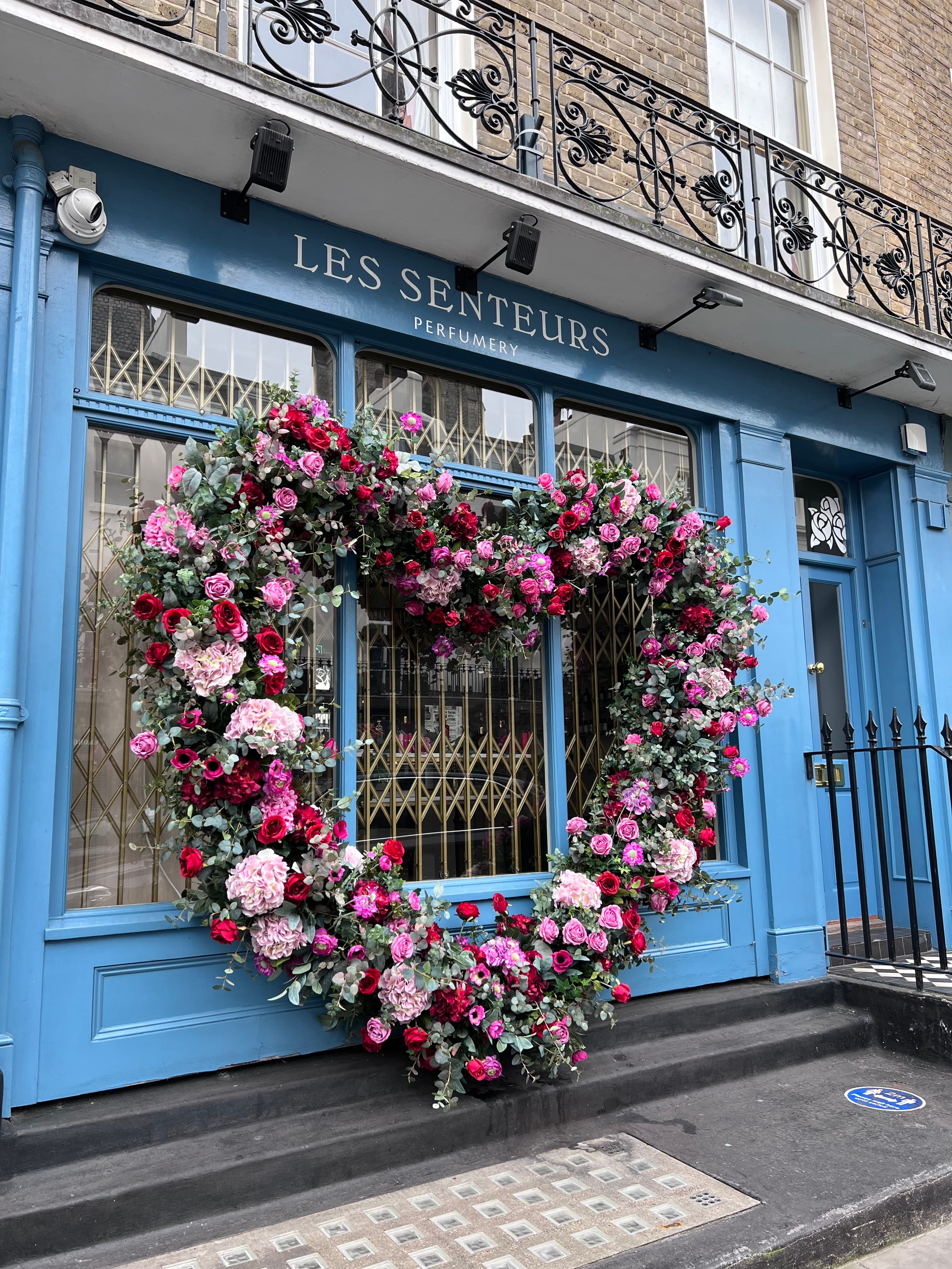 View of pink and red flowers in a large heart shape on a blue storefront