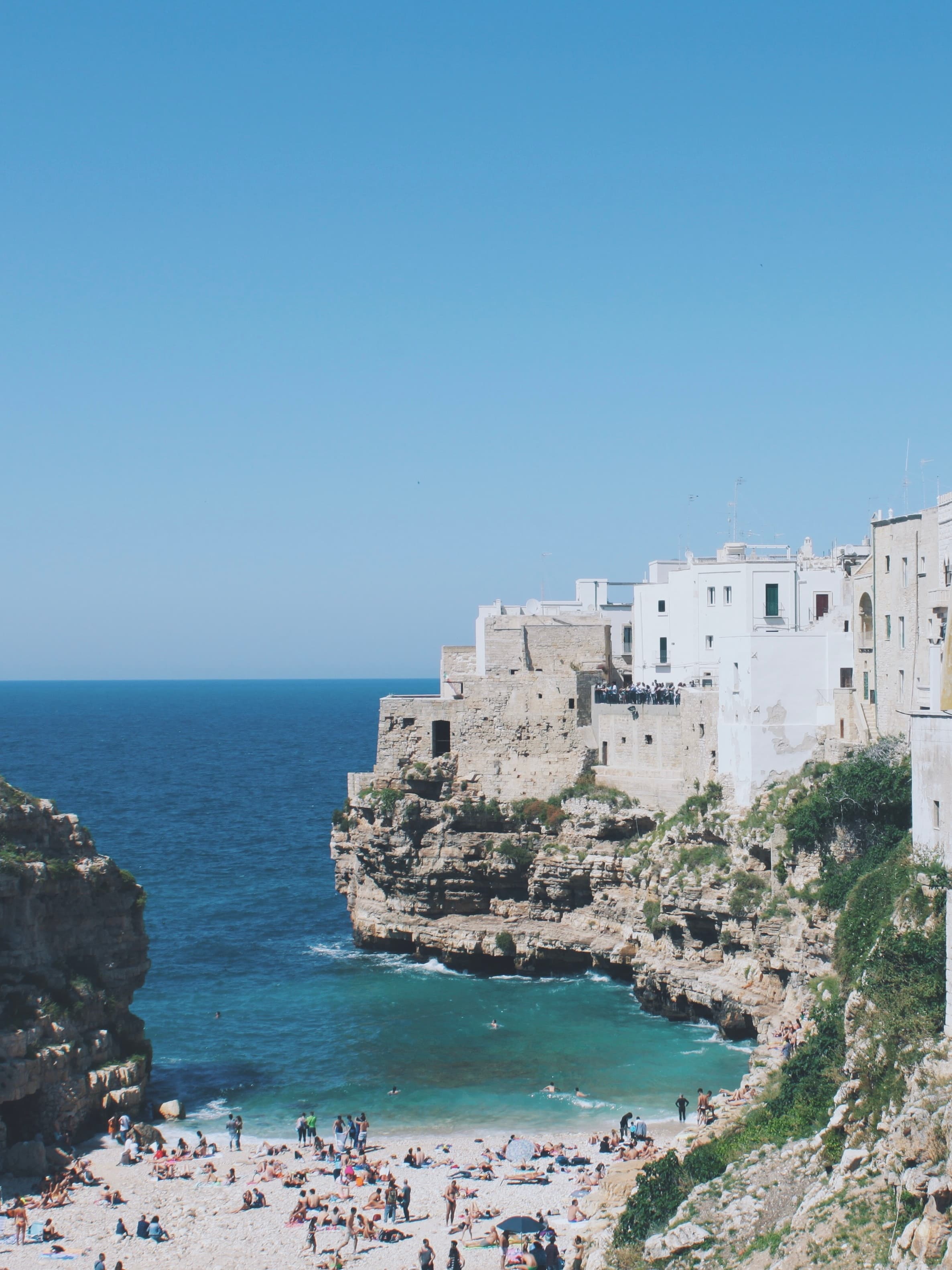 View of a small beach with sunbathers and a coastal town with old white buildings on the cliff beyond