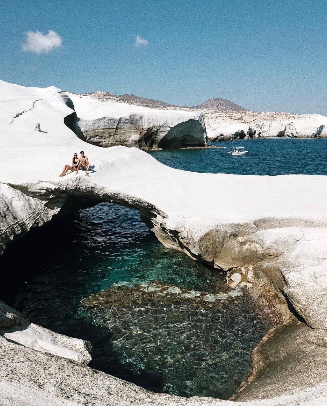 Advisor and partner sitting on a rock bridge formation over a deep blue sea