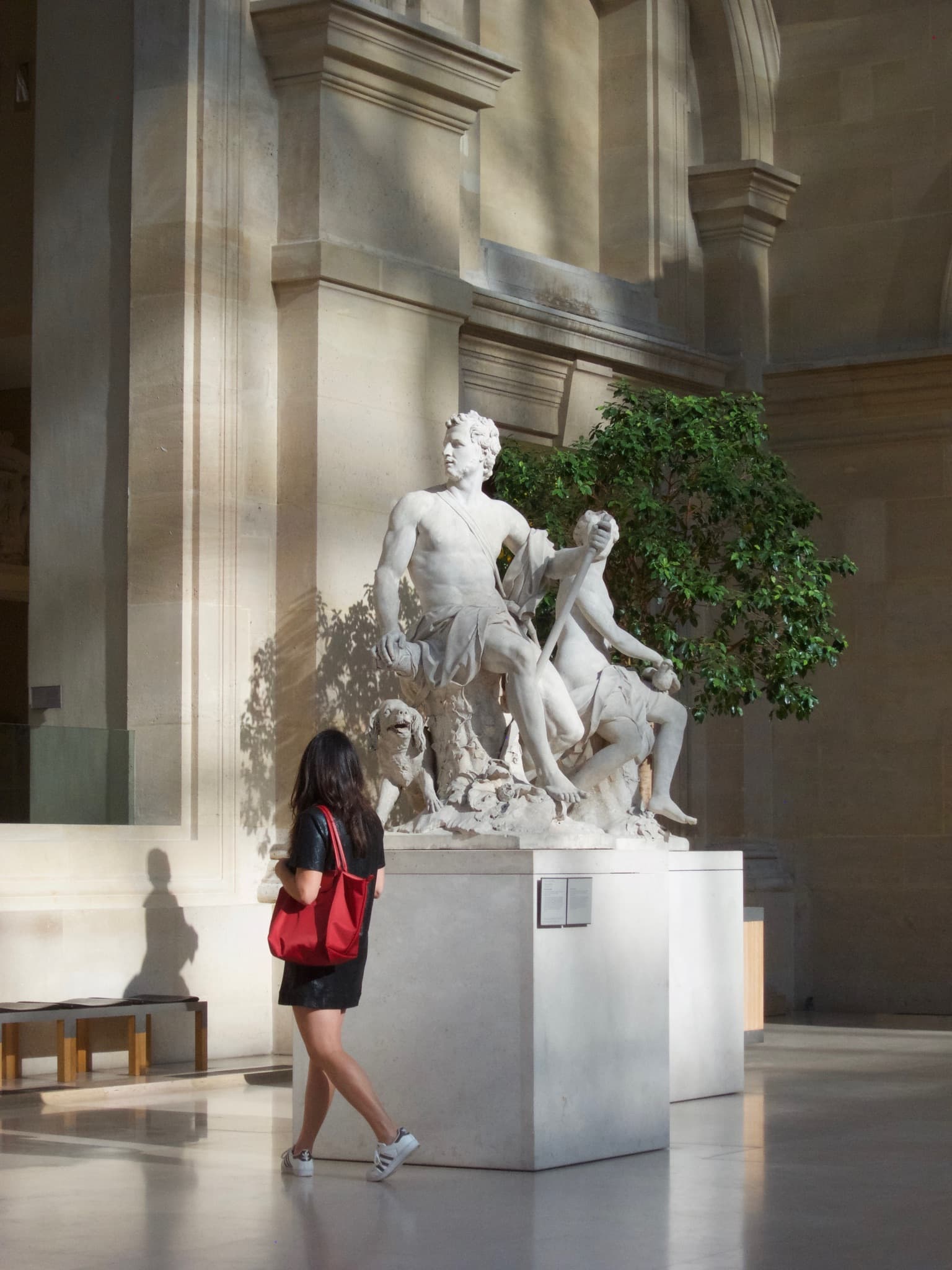 Woman with a red purse walking by a white marble sculpture in a museum