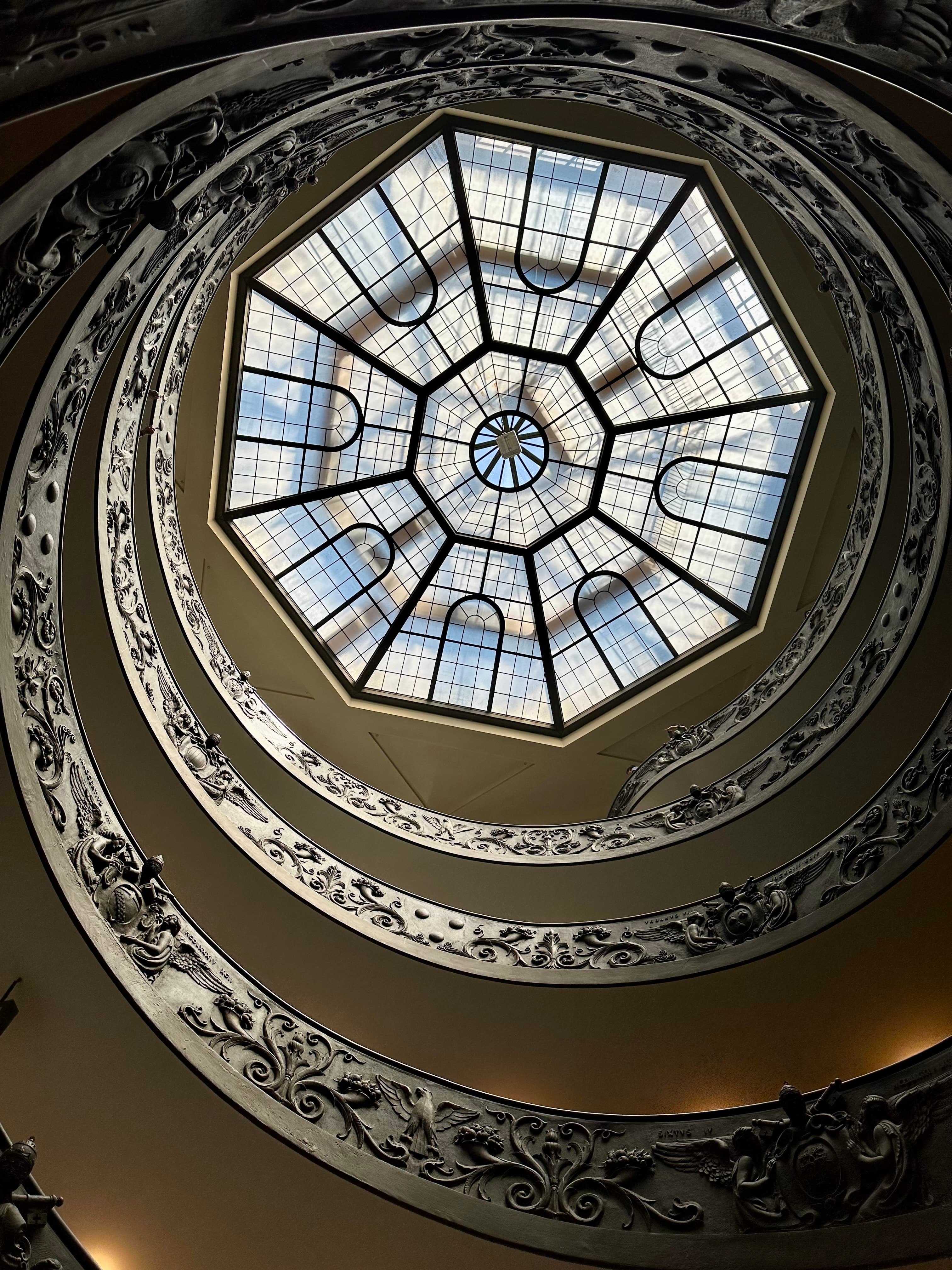 View of a circular window in the ceiling of a building, a spiral staircase leading upwards towards it