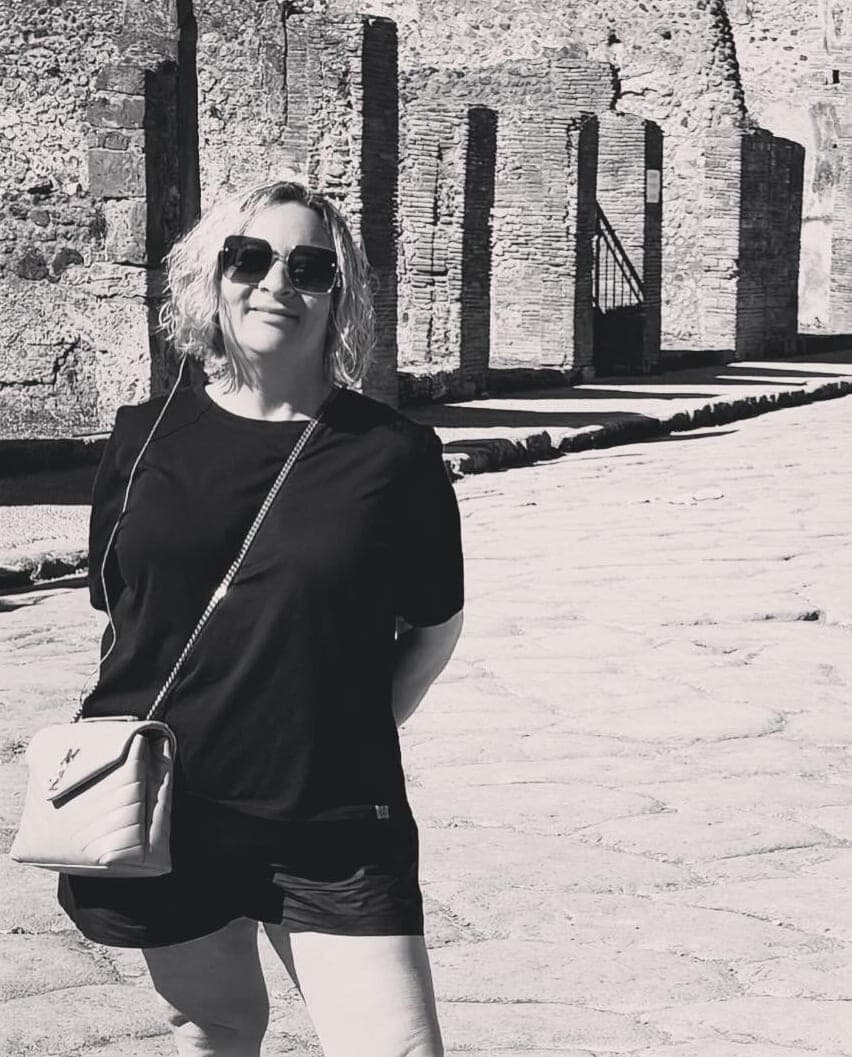 Black and white image of advisor posing on a sunny street with old stone structures behind her