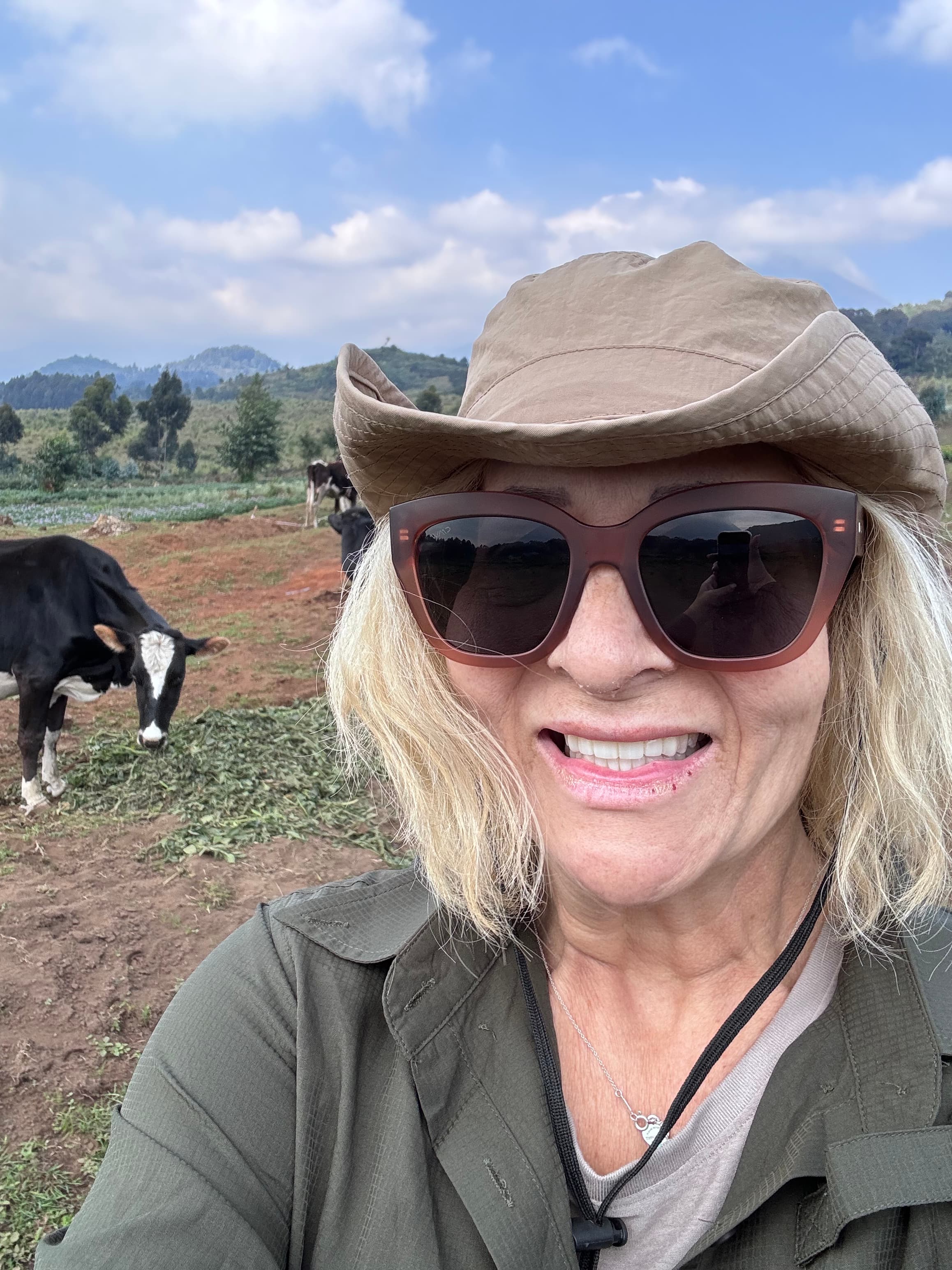Advisor smiling for a selfie in large sunglasses with a black cow grazing in the background