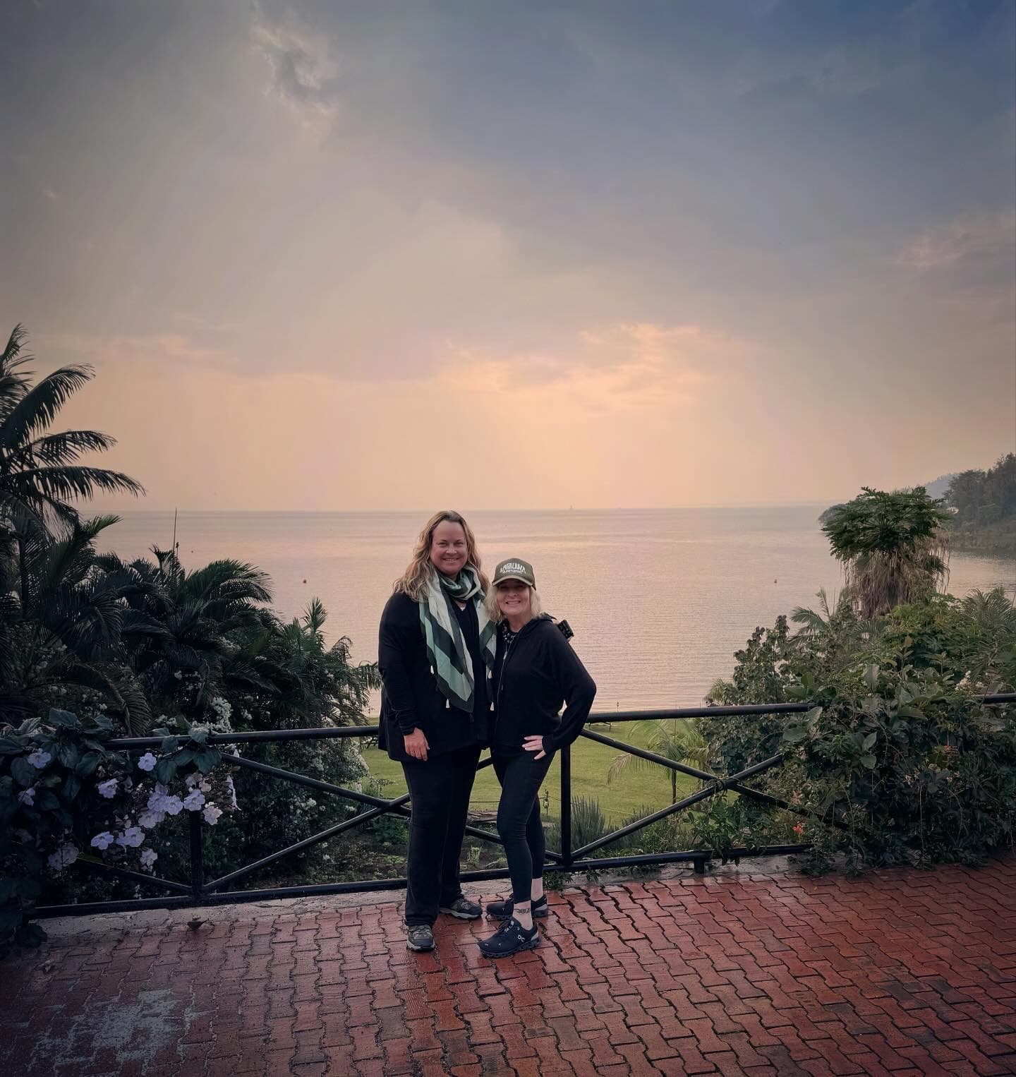 Advisor and a friend smiling side by side on a balcony overlooking the sea on a cloudy evening