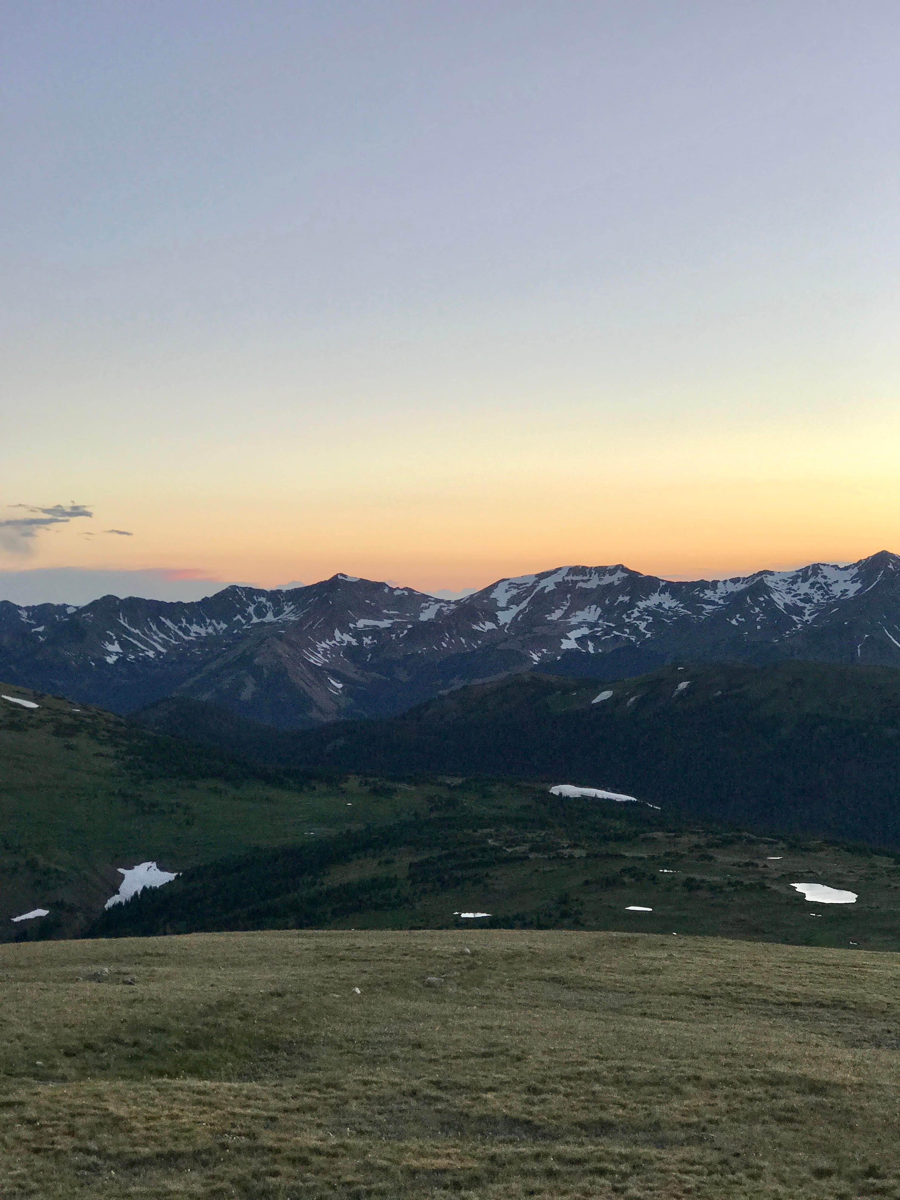 View of a field and distant mountain range with pale orange sunlight above