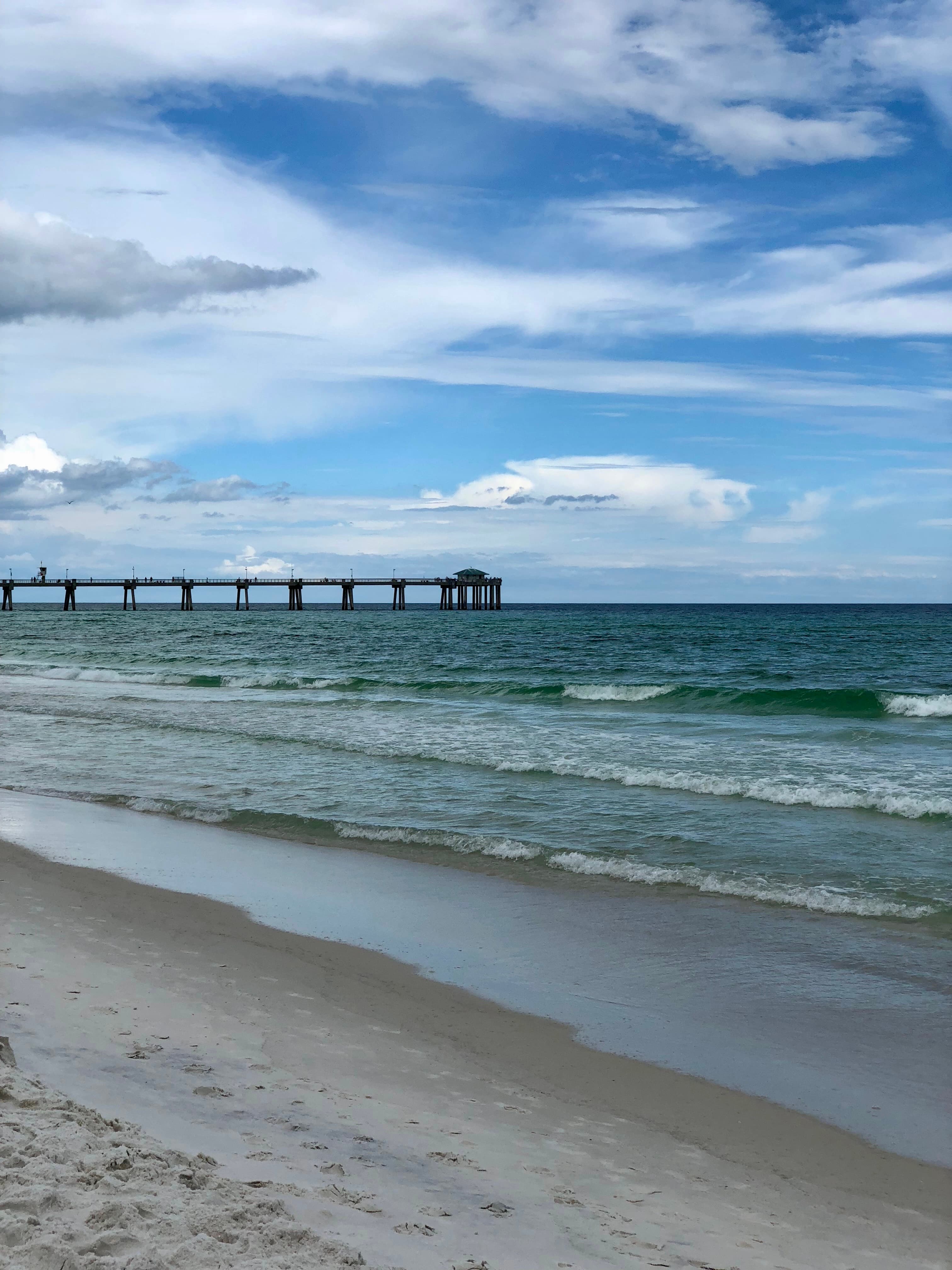 Small waves washing ashore on a sandy beach with a large pier visible in the distance