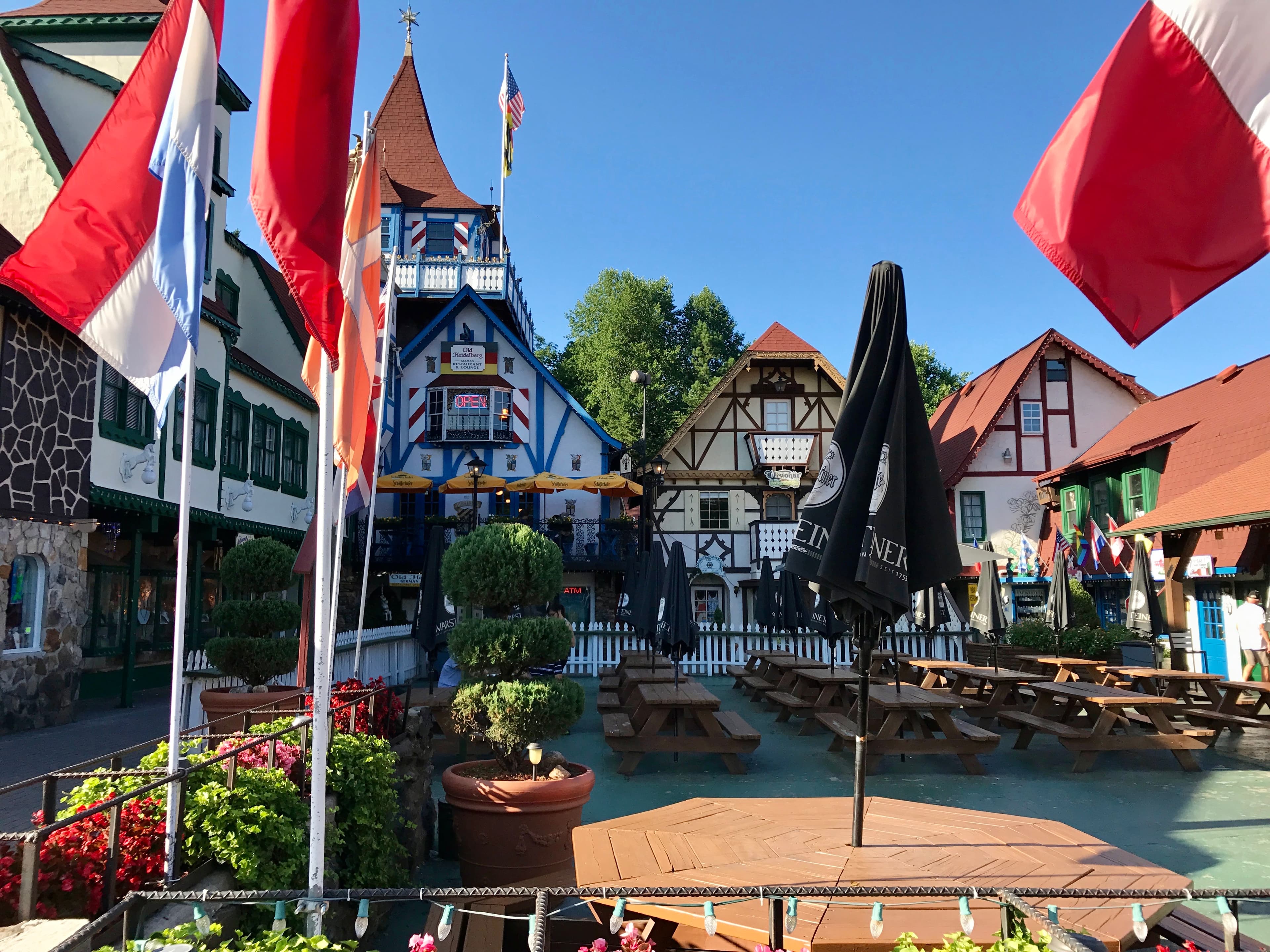 View of flags and picnic tables surrounded by white buildings with exposed wooden beams on a sunny day