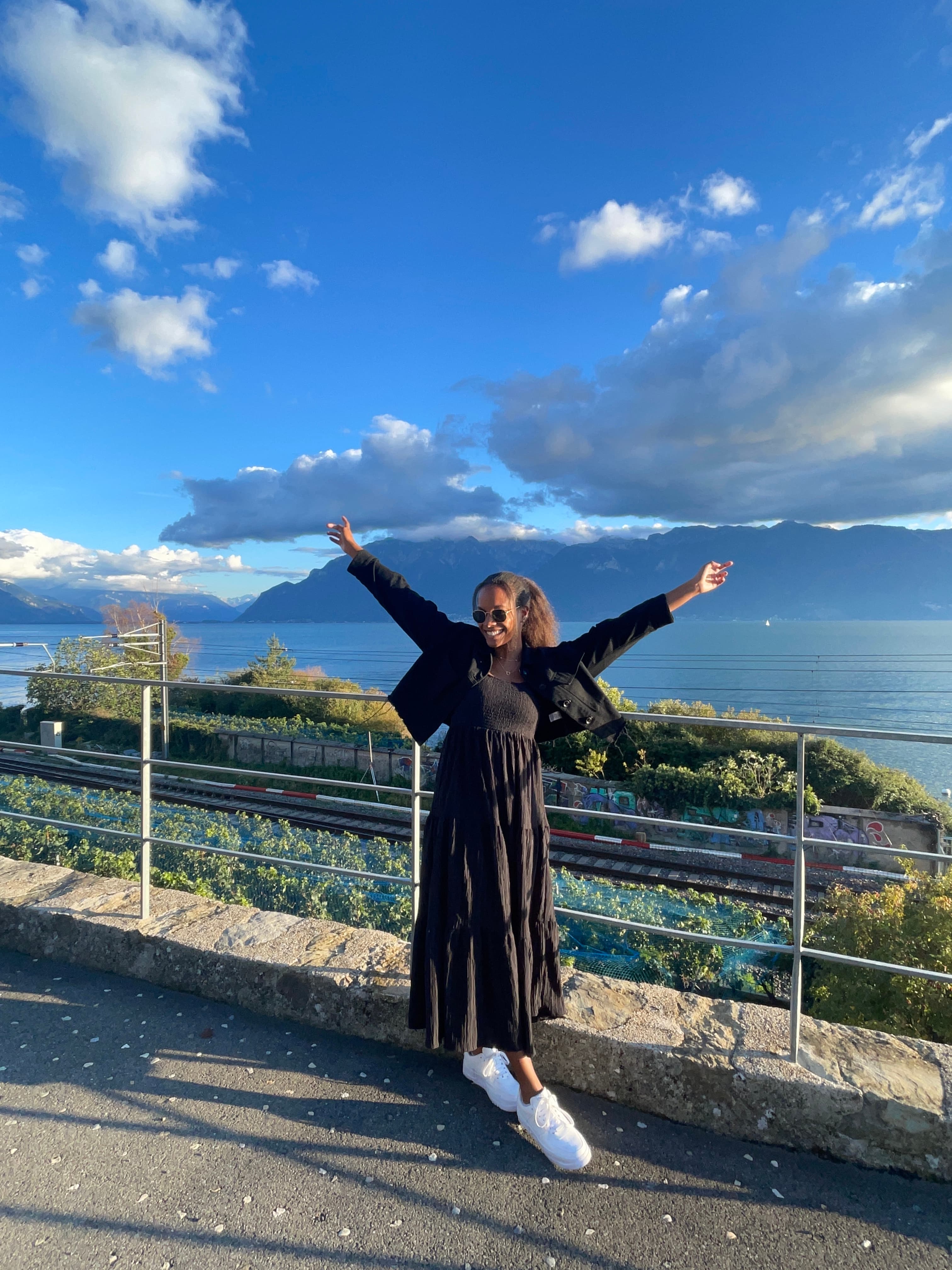 Advisor posing with arms raised at a viewpoint overlooking a sunny coastline and distant mountains