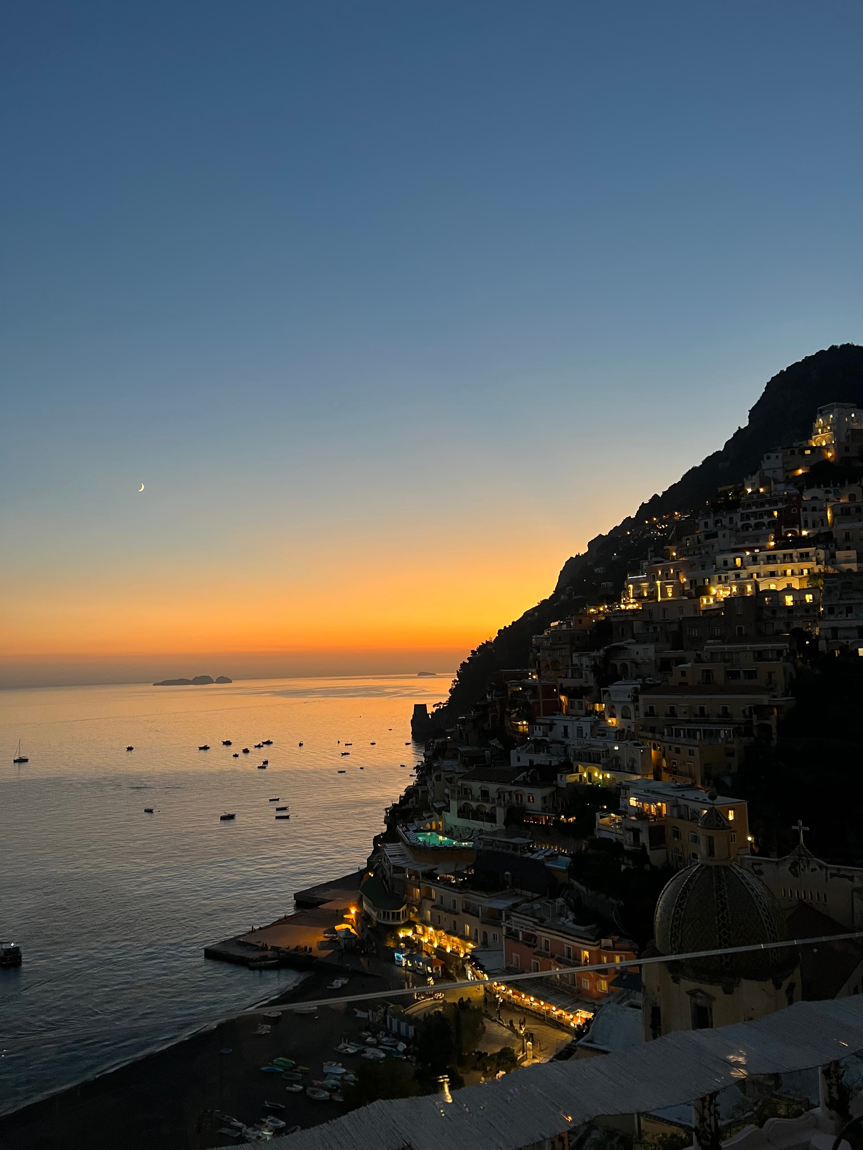 Beautiful aerial view of sunset over a coastal city and a calm sea with boats floating offshore