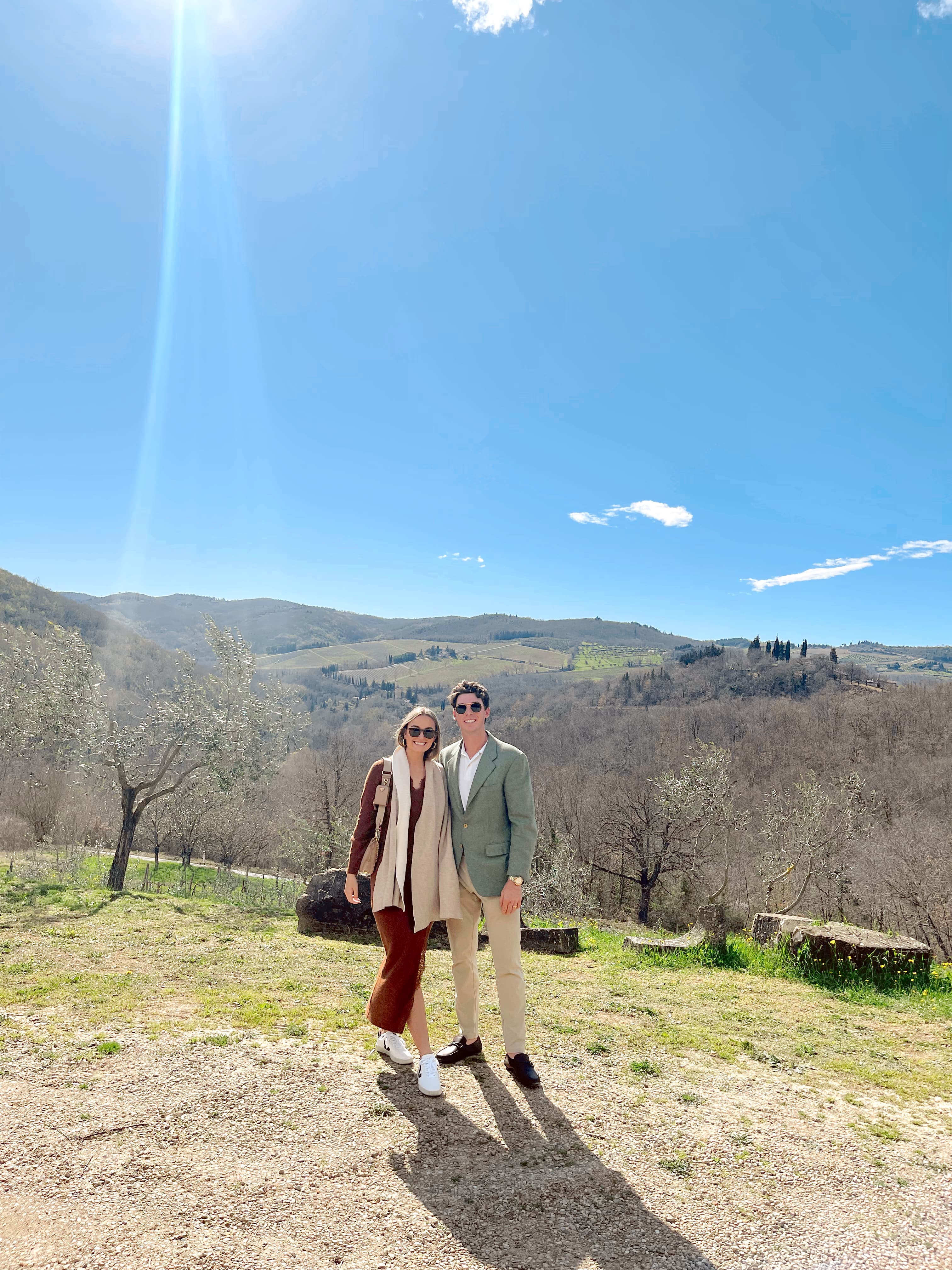 Advisor and partner smiling side by side on a grassy hill overlooking distant trees on a clear day