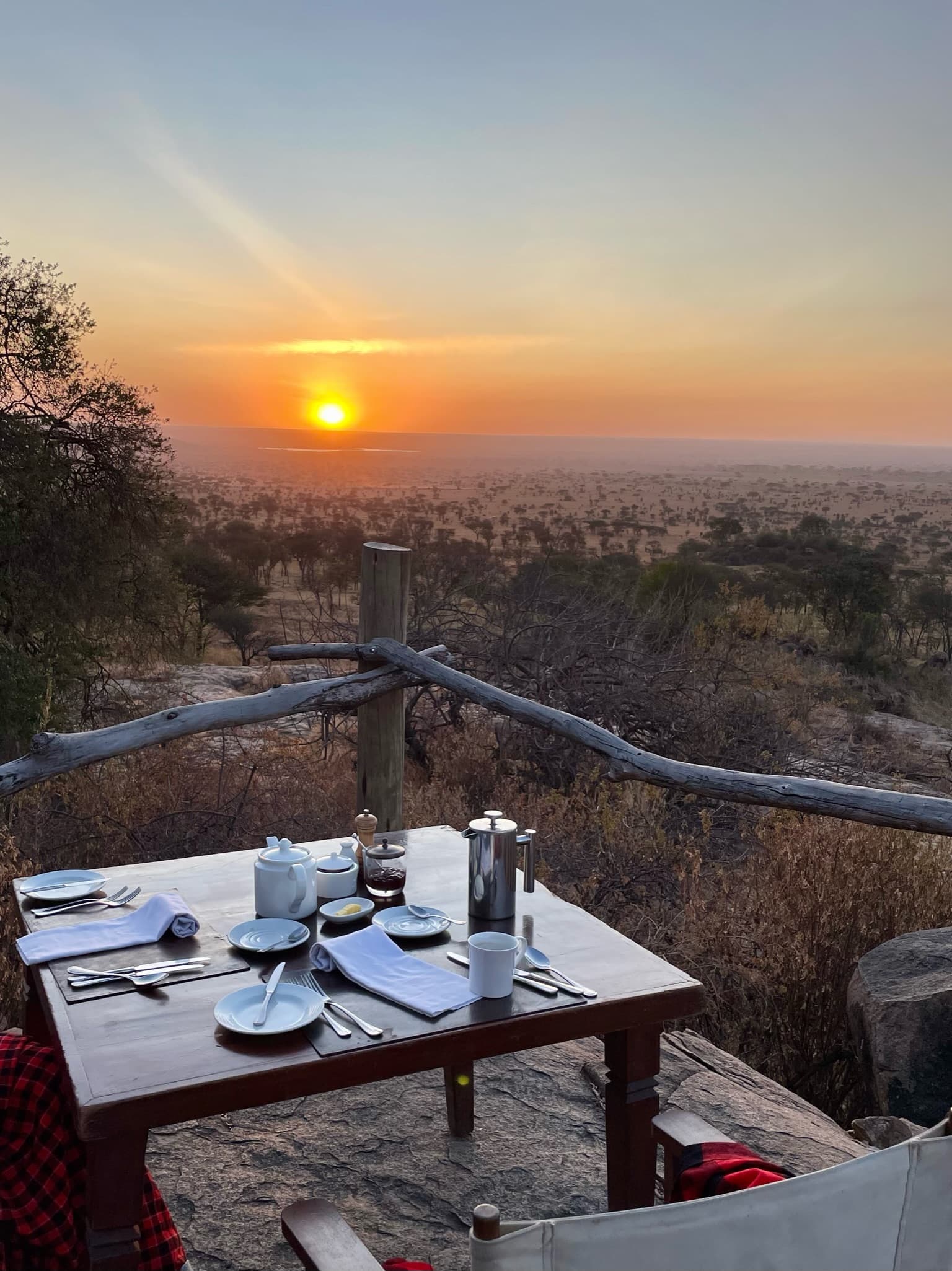 View of a table set with plates and napkins outdoors with a sunset over the horizon