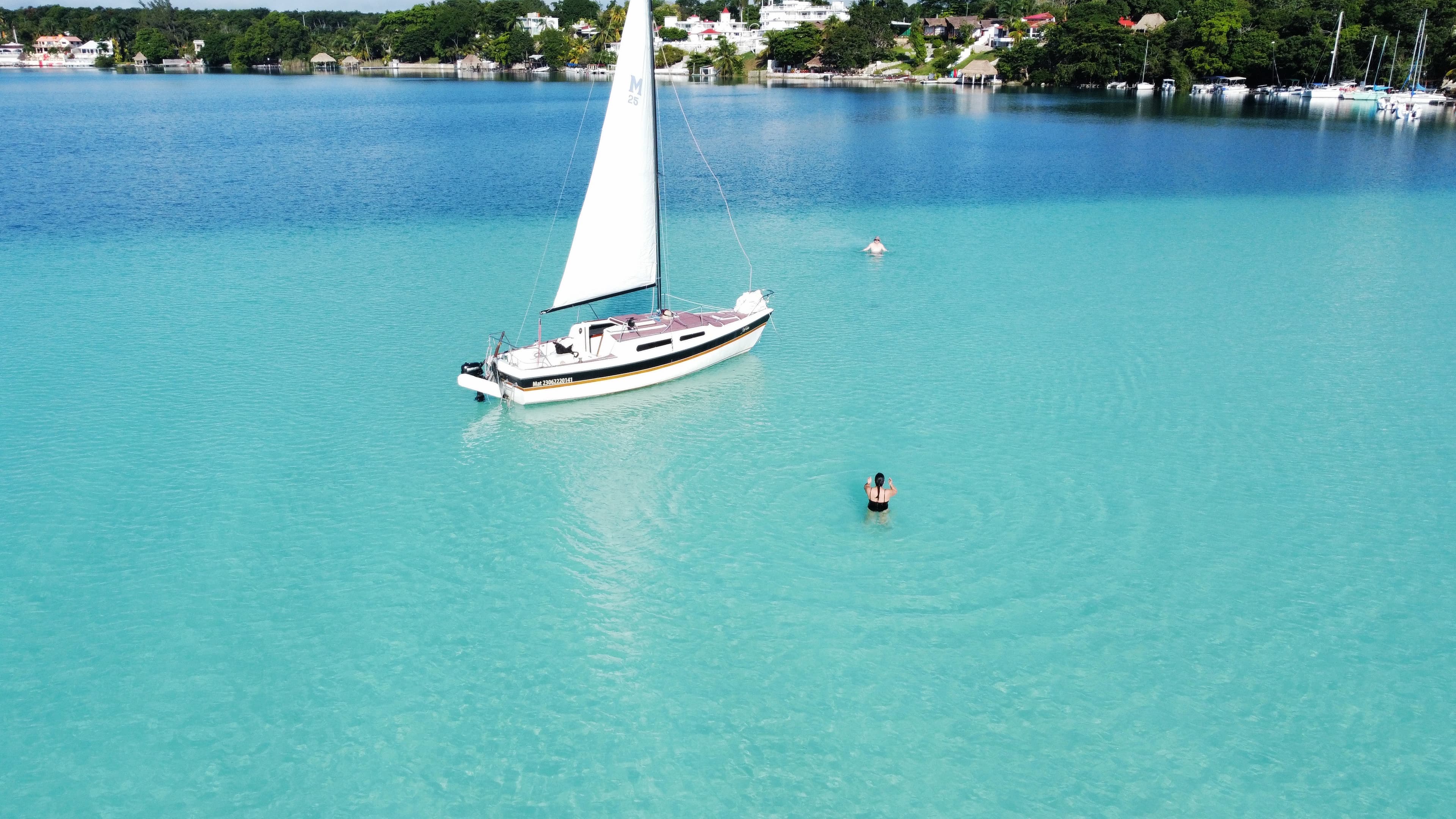 Overhead view of a person in crystal clear turquoise water with a sailboat anchored nearby