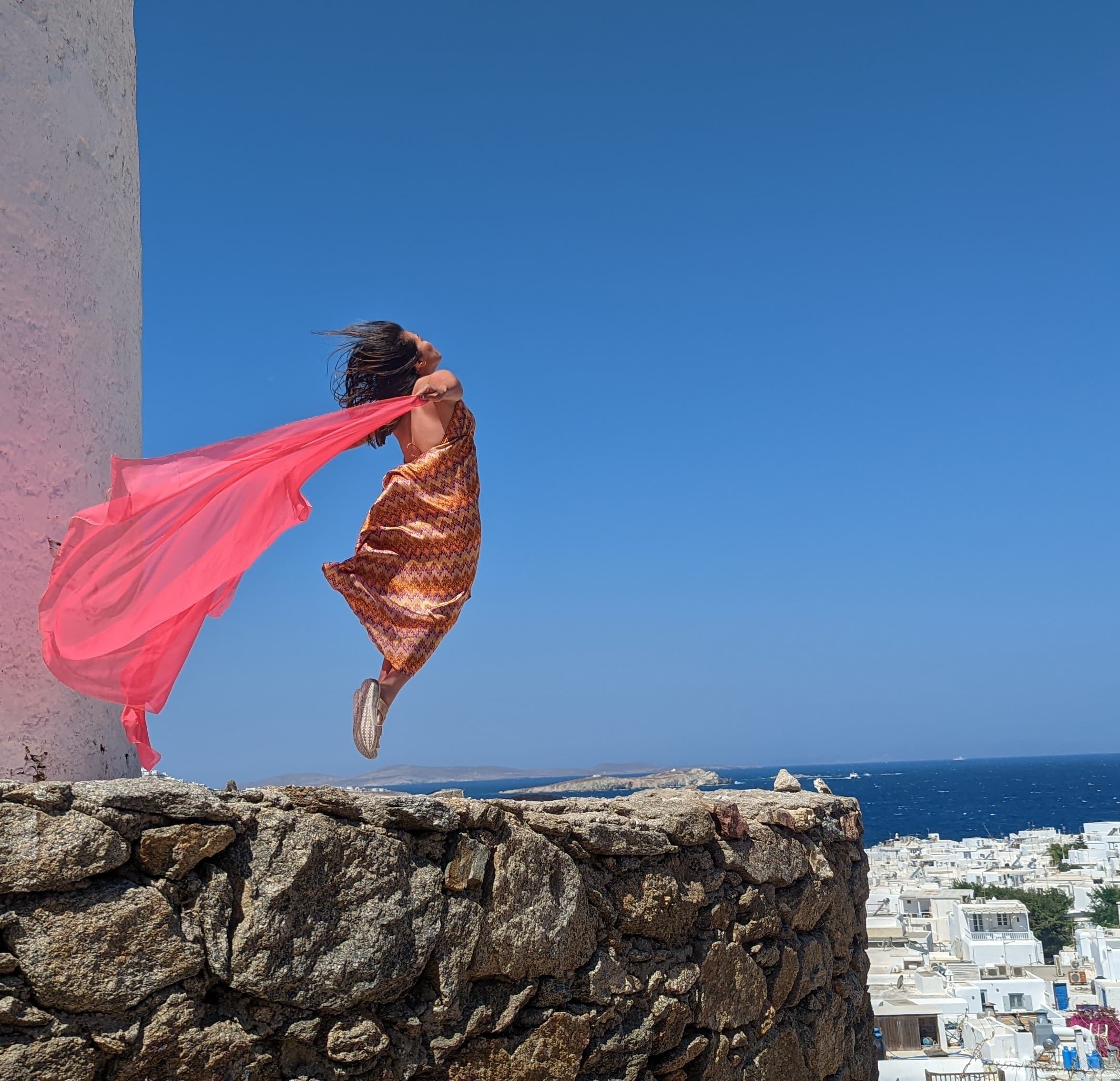 Image of advisor jumping in midair with a long red scarf in the wind behind her on a sunny day