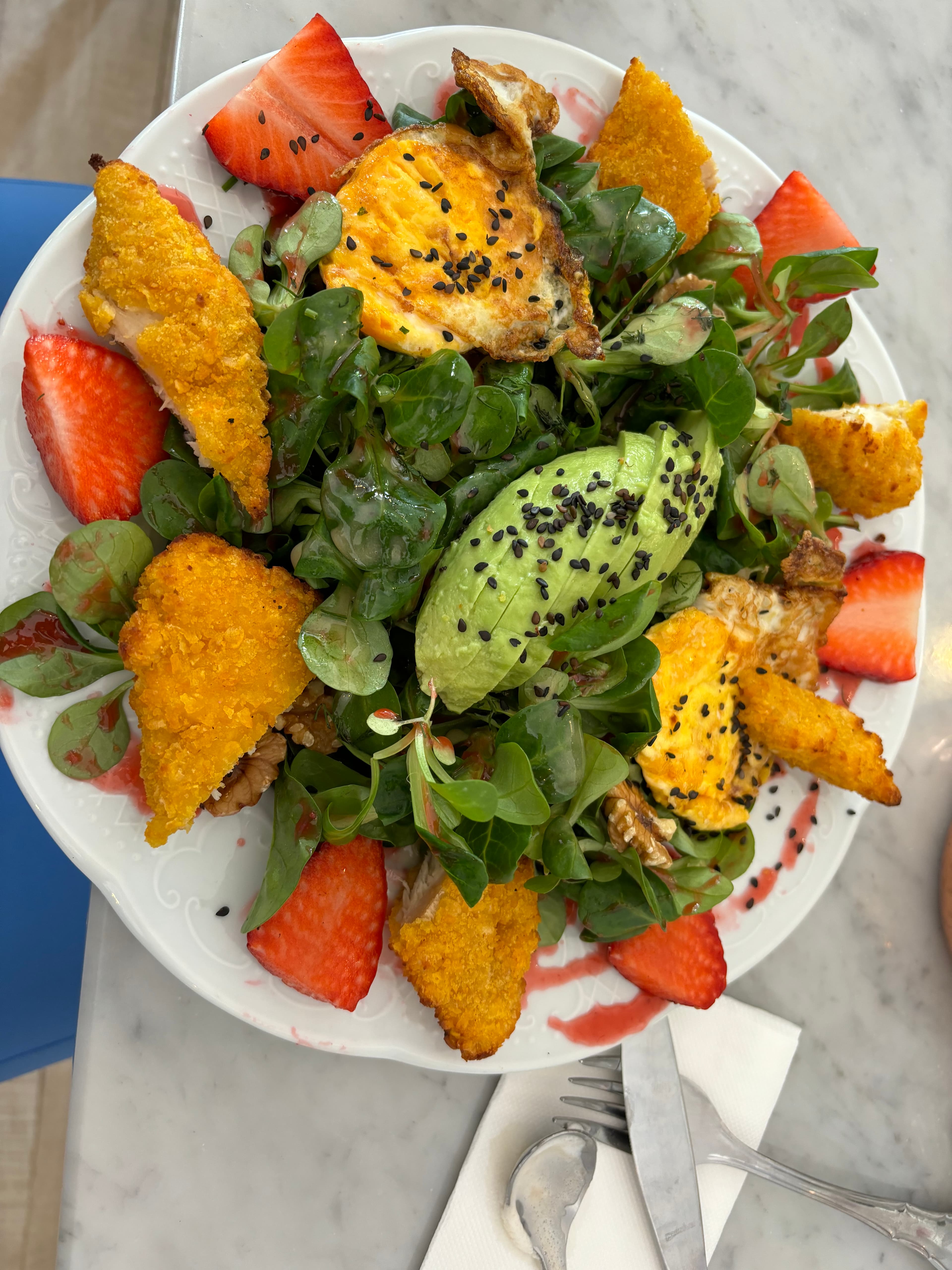 A white plate of a salad with red and orange fruit