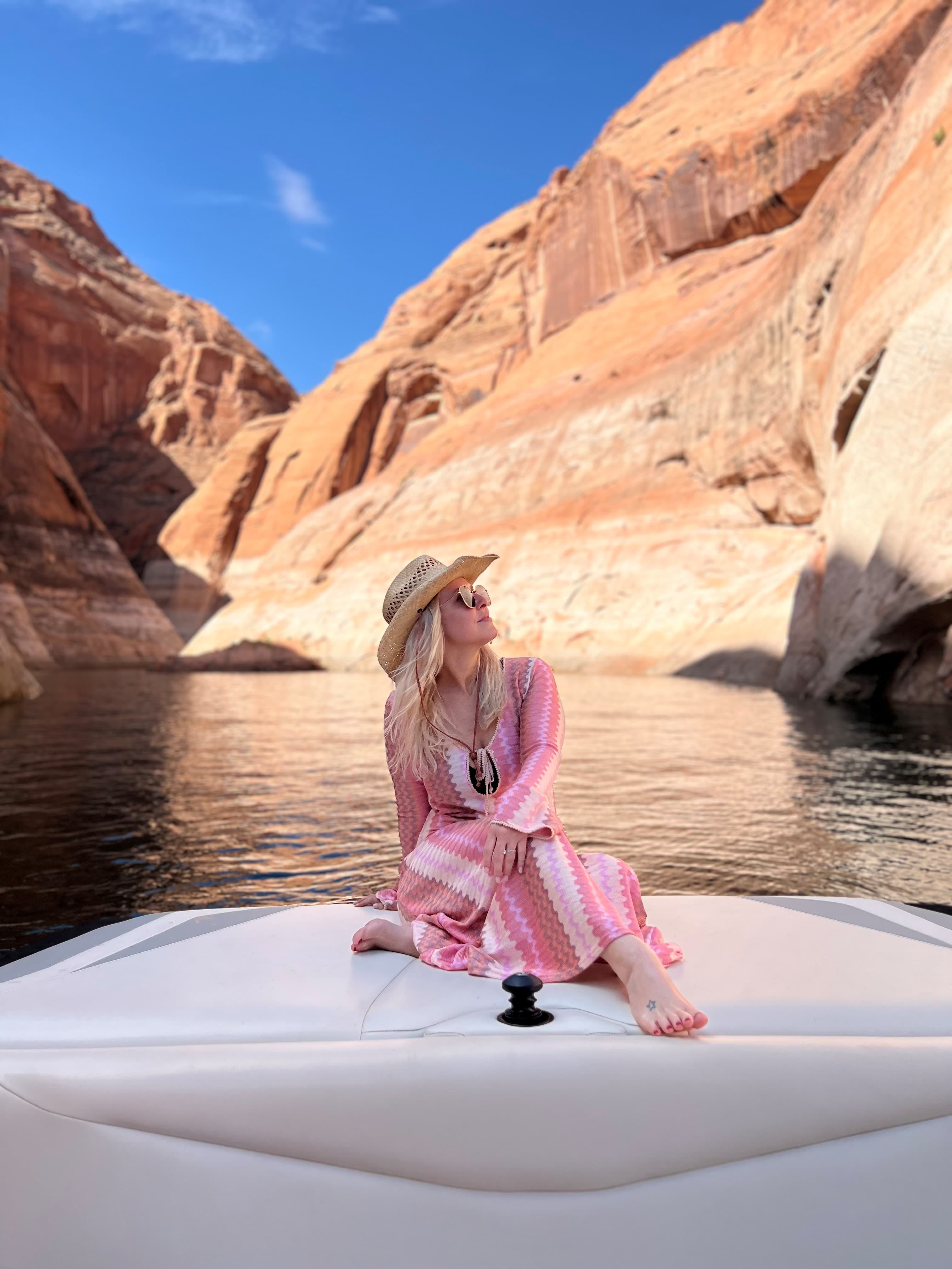 Advisor in a pink and white dress sitting on the front of a boat with cliffs in the background on a clear day