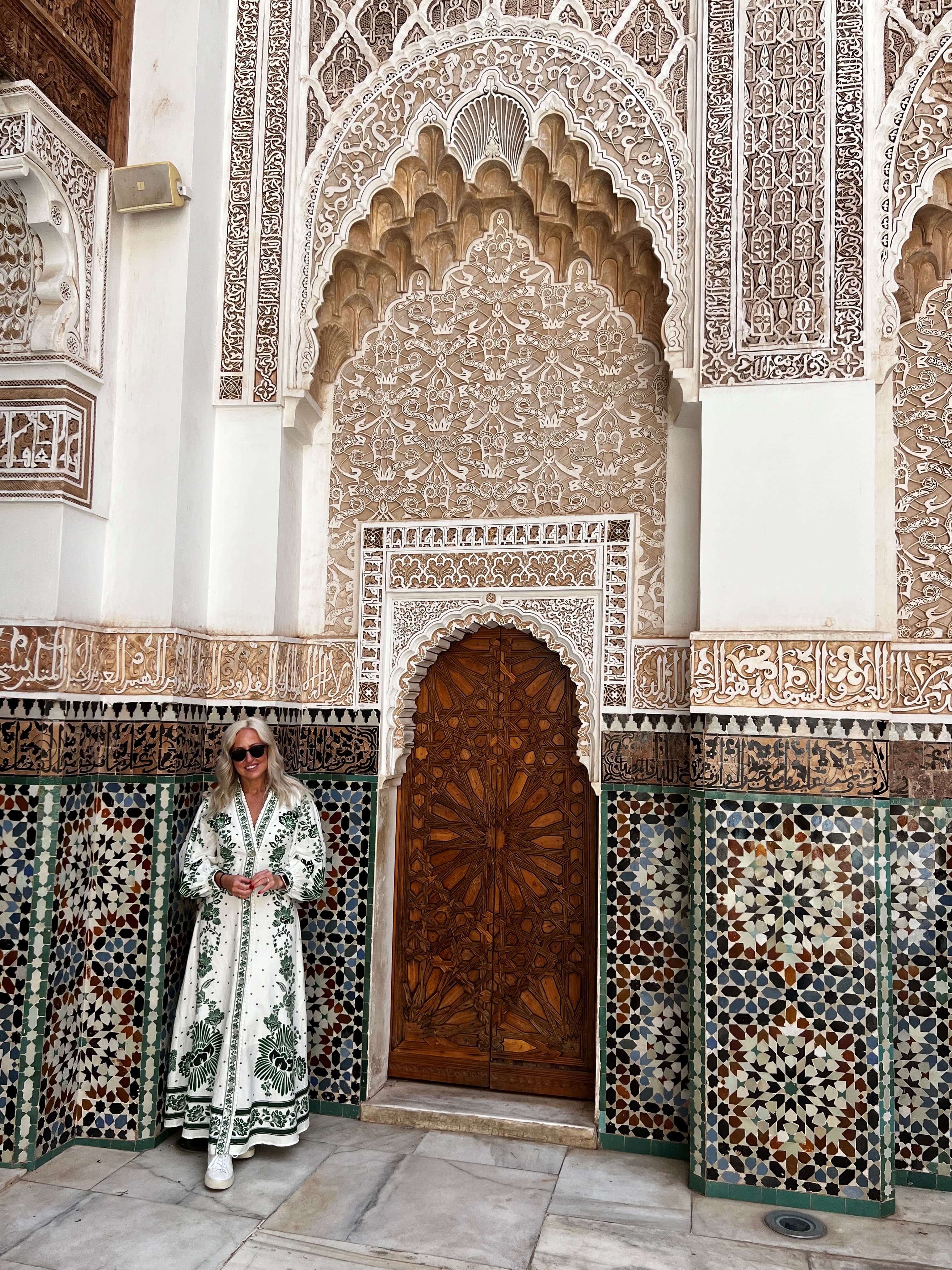 Advisor in a long white dress with green embroidery by an ornately designed building with Arabic influence