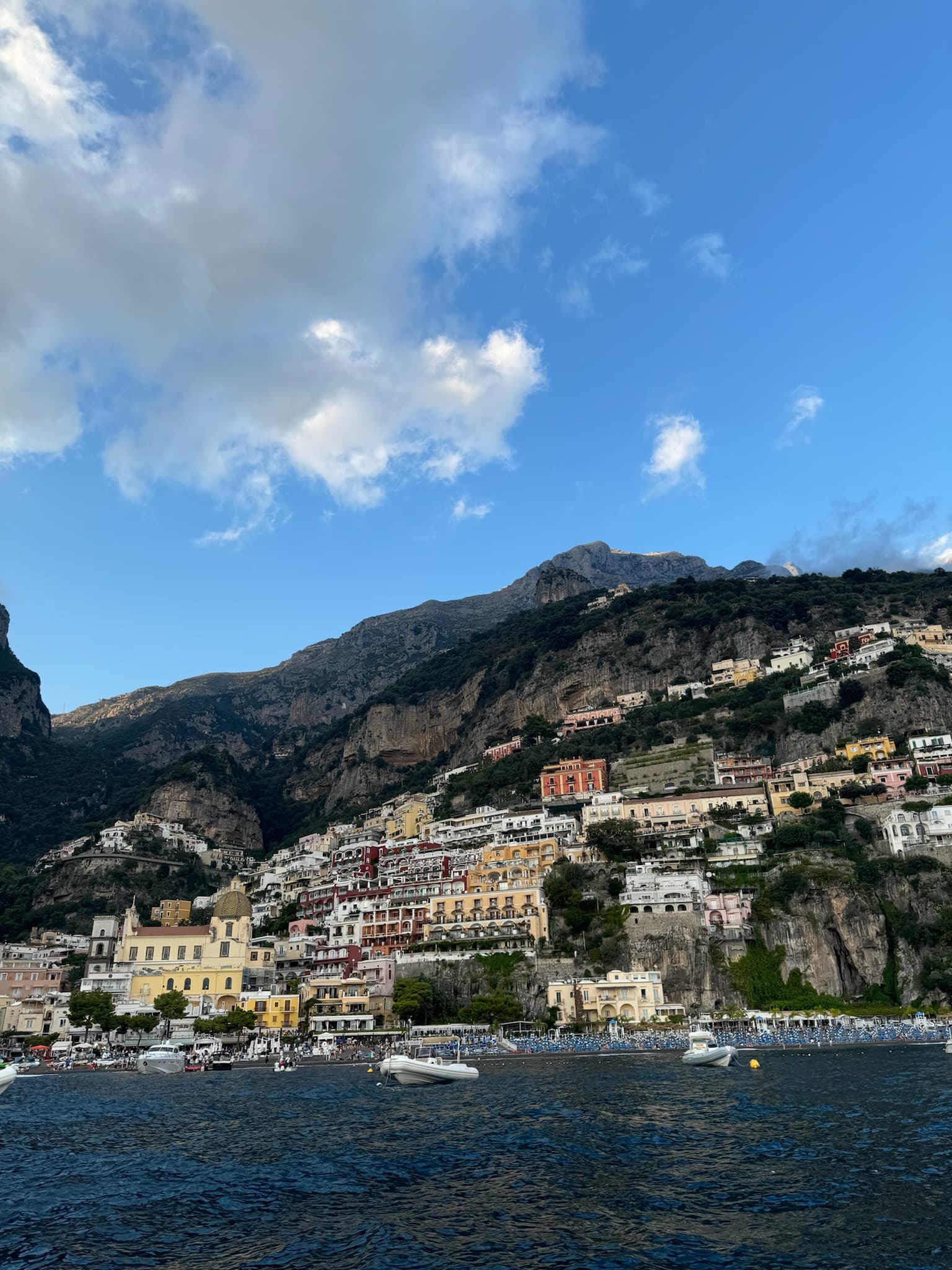 View from a boat of a colorful coastal town rising on a hill above a deep blue sea