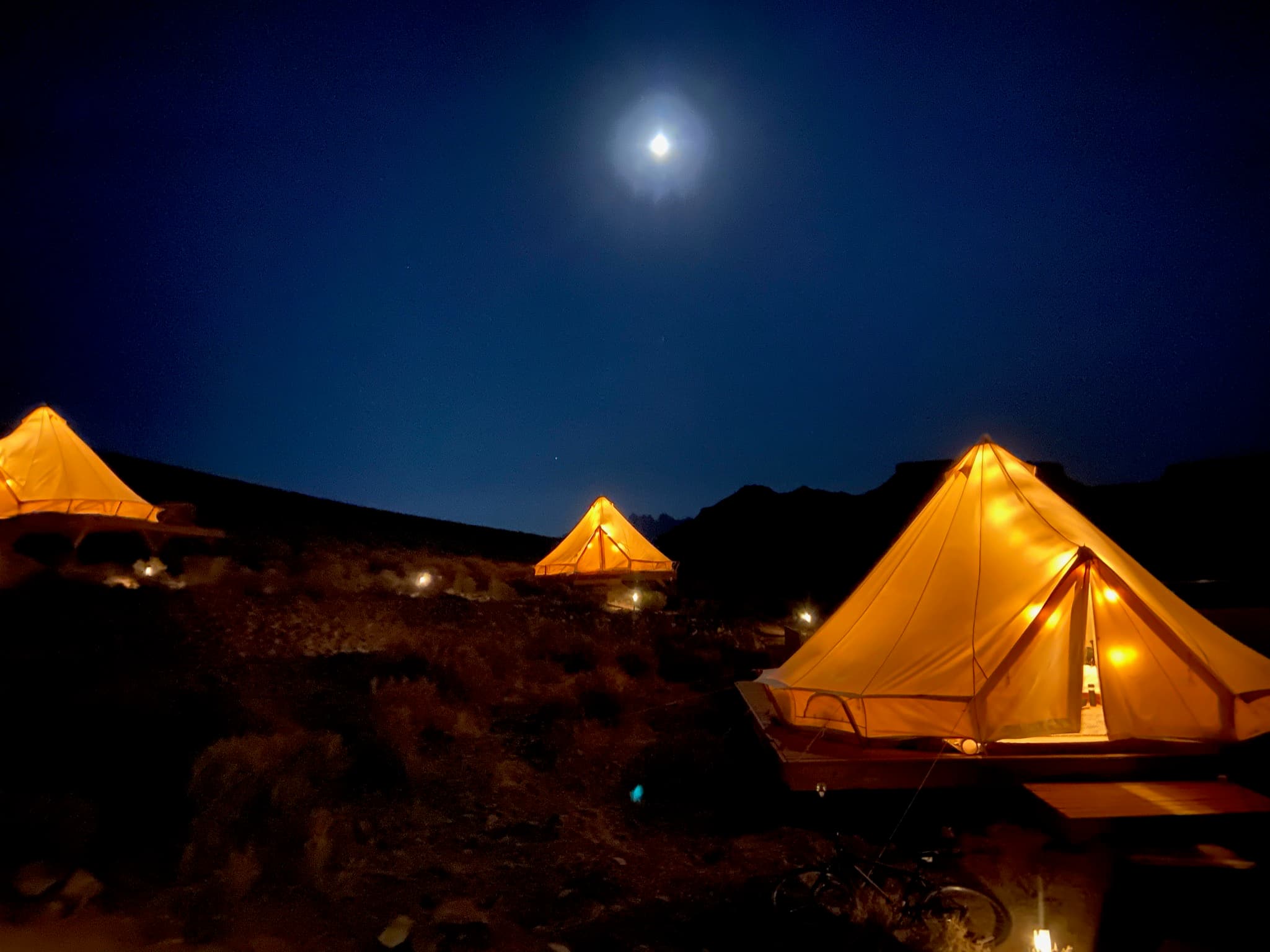 View of three glamping tents lit up at night under a full moon