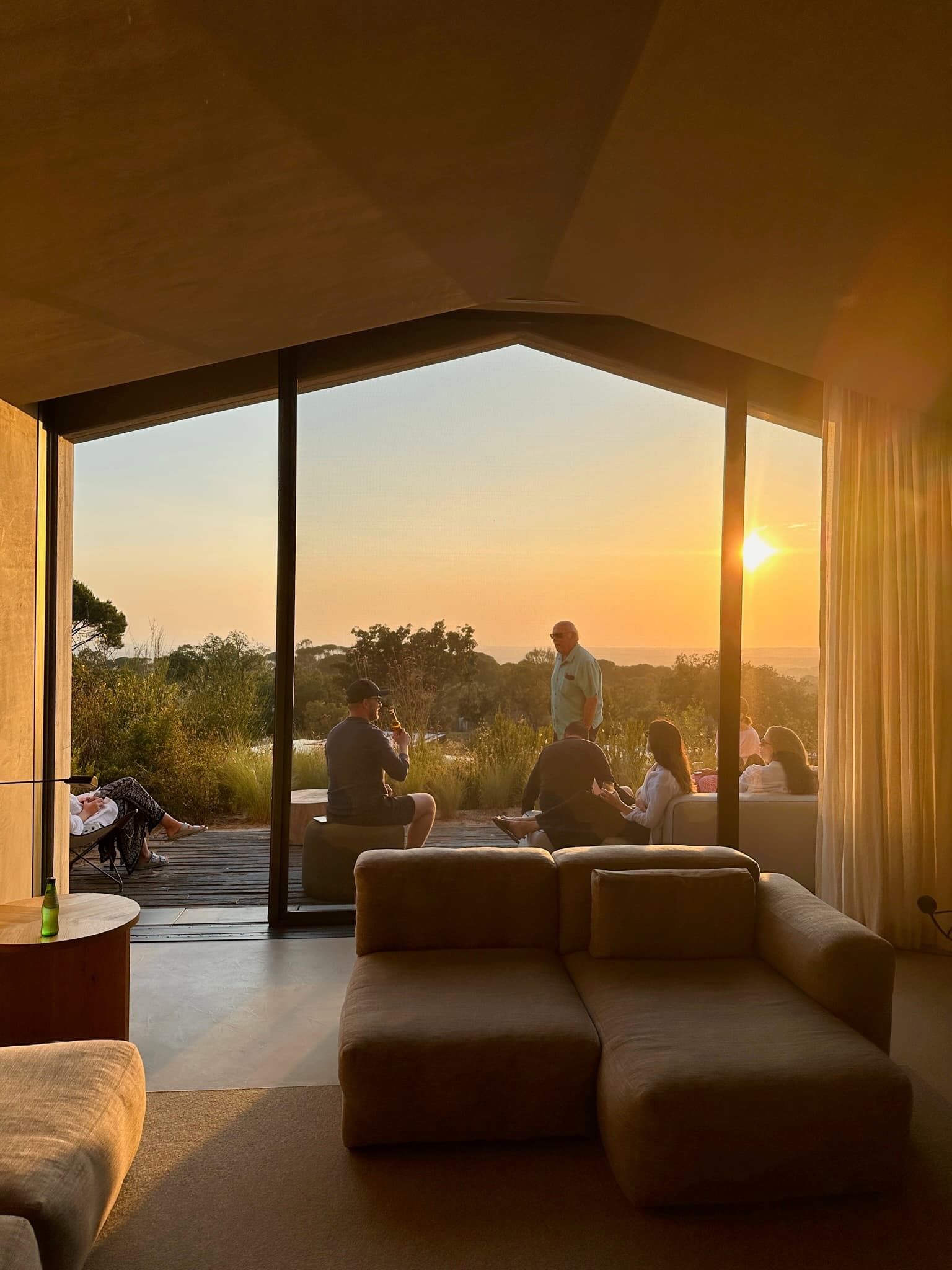 View of a group of people sitting and enjoying sunset seen through a large glass window