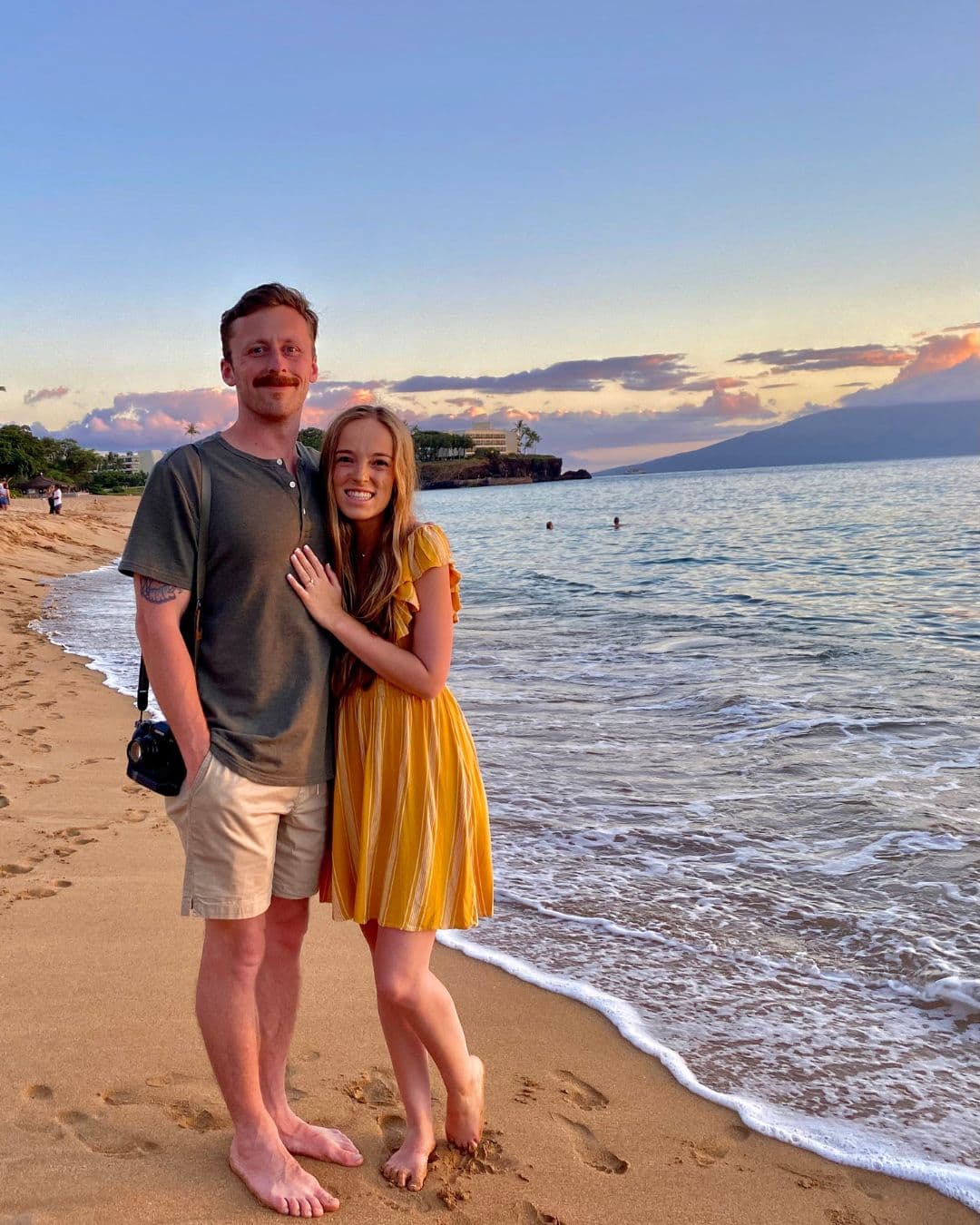 Advisor and partner smiling side by side at the ocean’s edge with a golden sunset behind them
