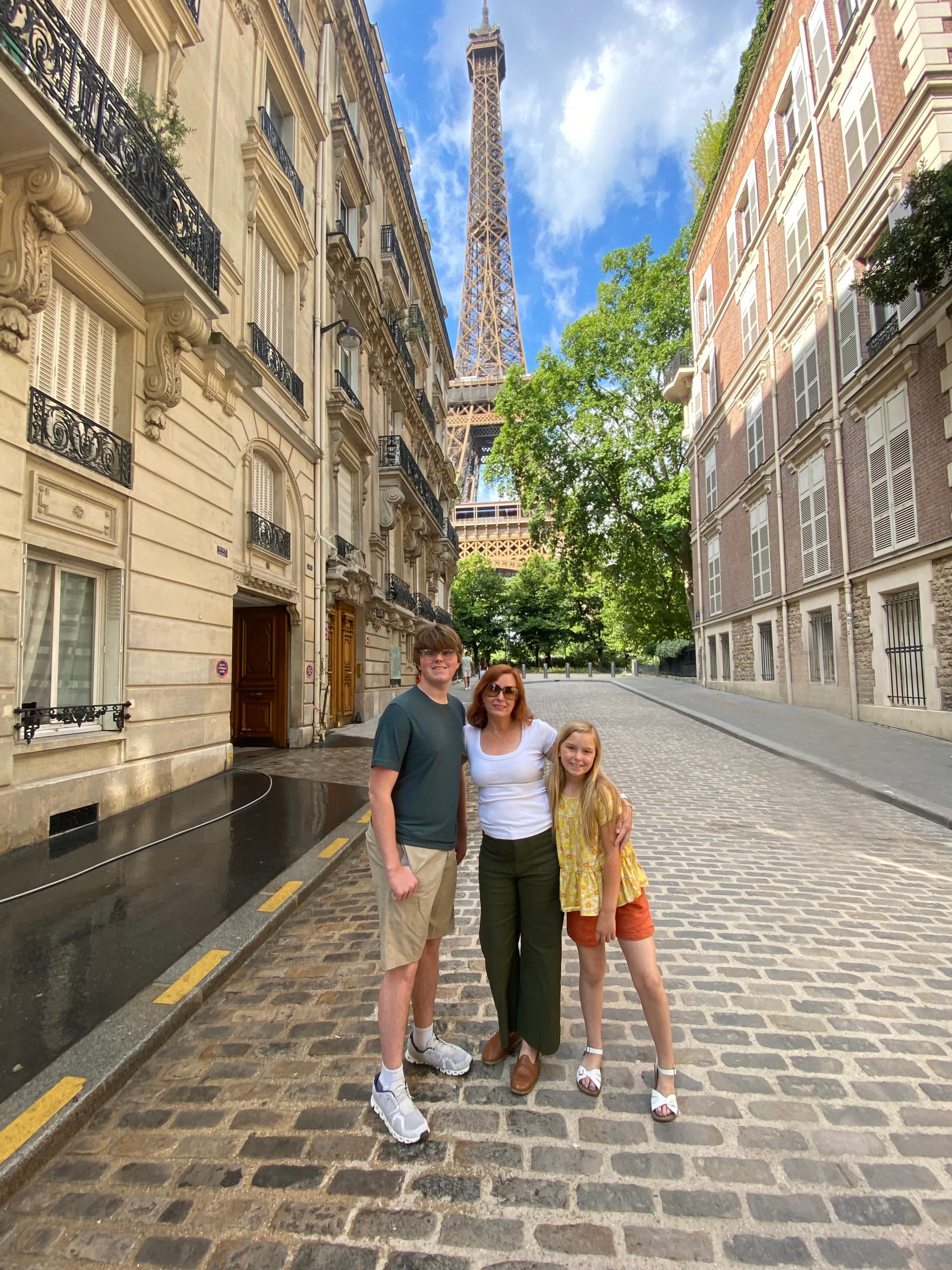 Advisor smiling side by side with her children on a street in Paris with the Eiffel Tower visible in the background