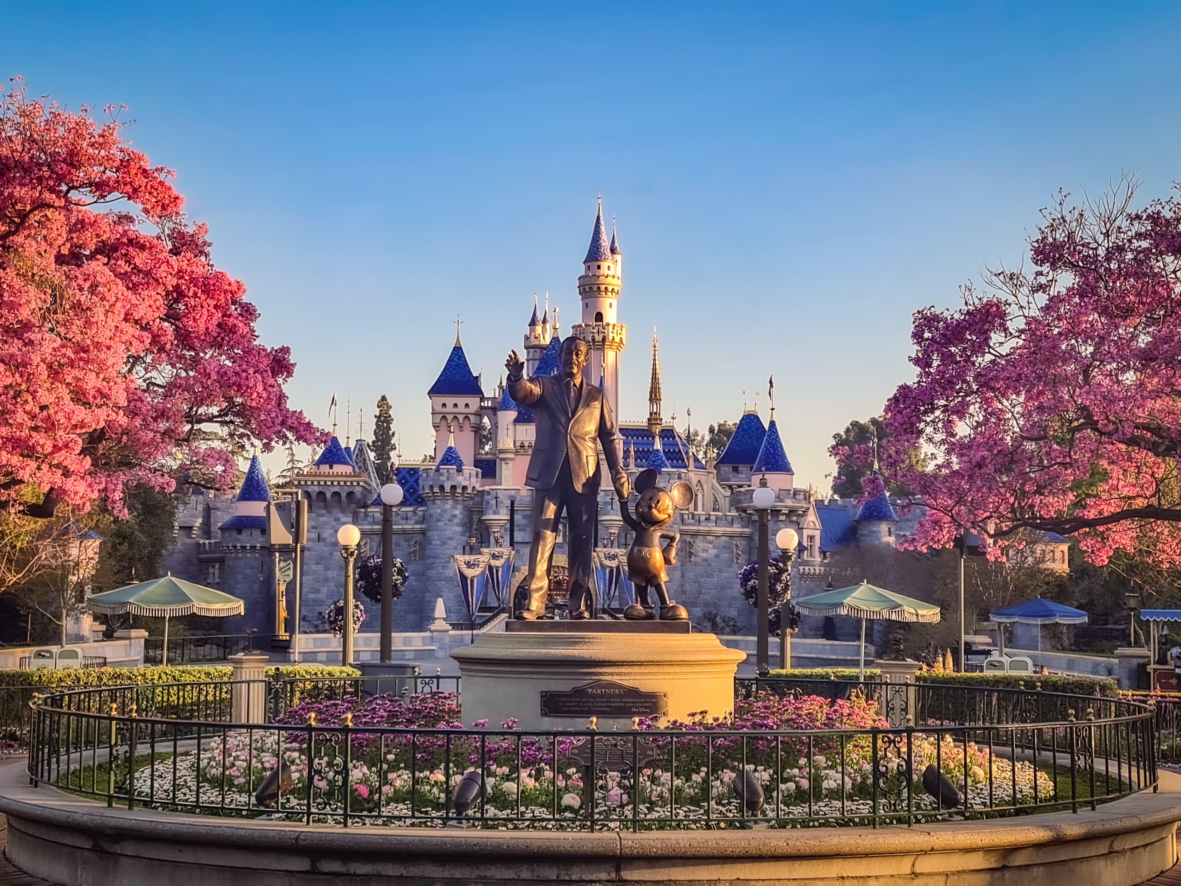 View Sleeping Beauty’s castle at Disneyland with metal statues of characters in the foreground