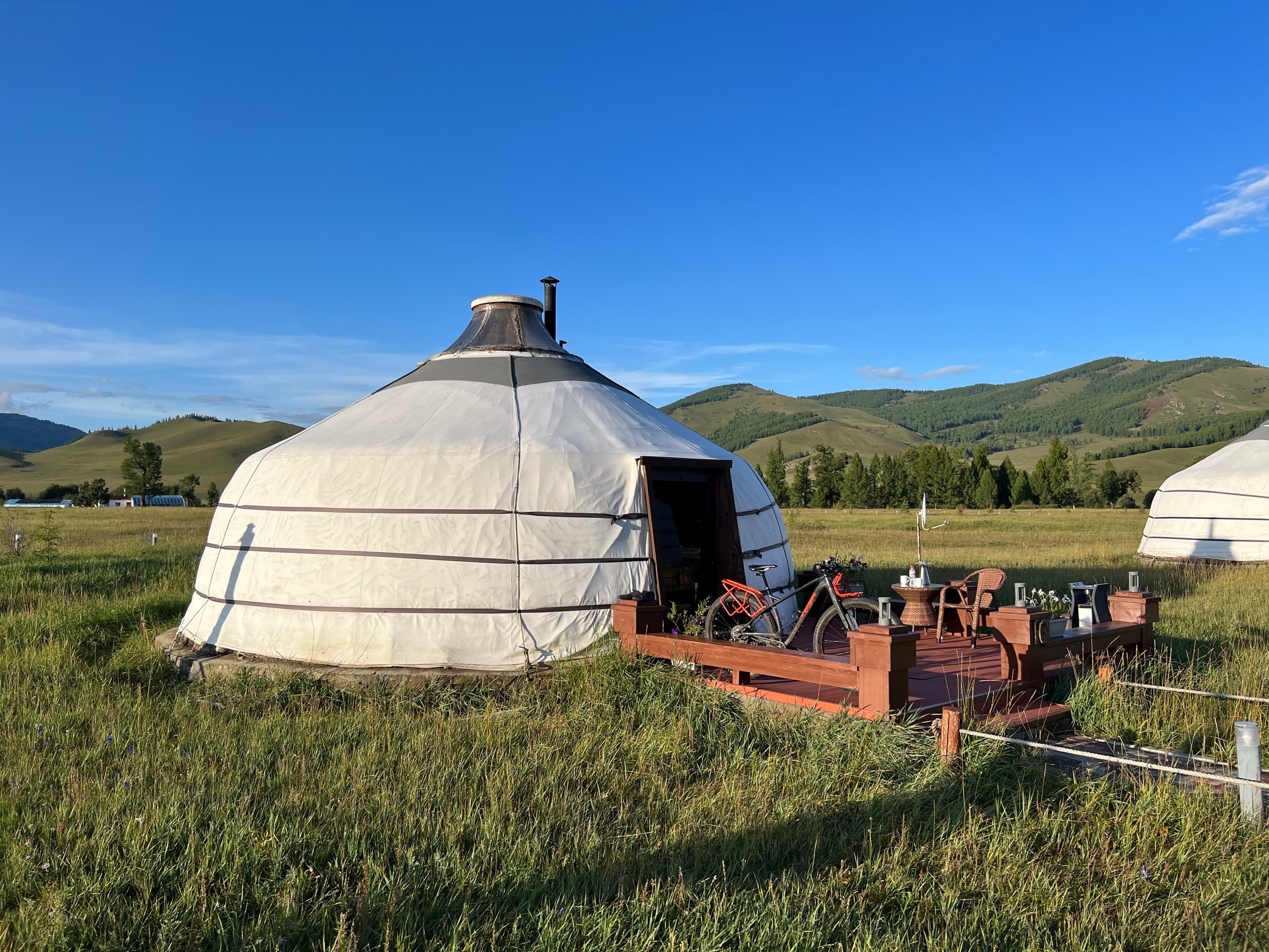 View of a white tent in a grassy field with rolling green hills in the distance on a clear day