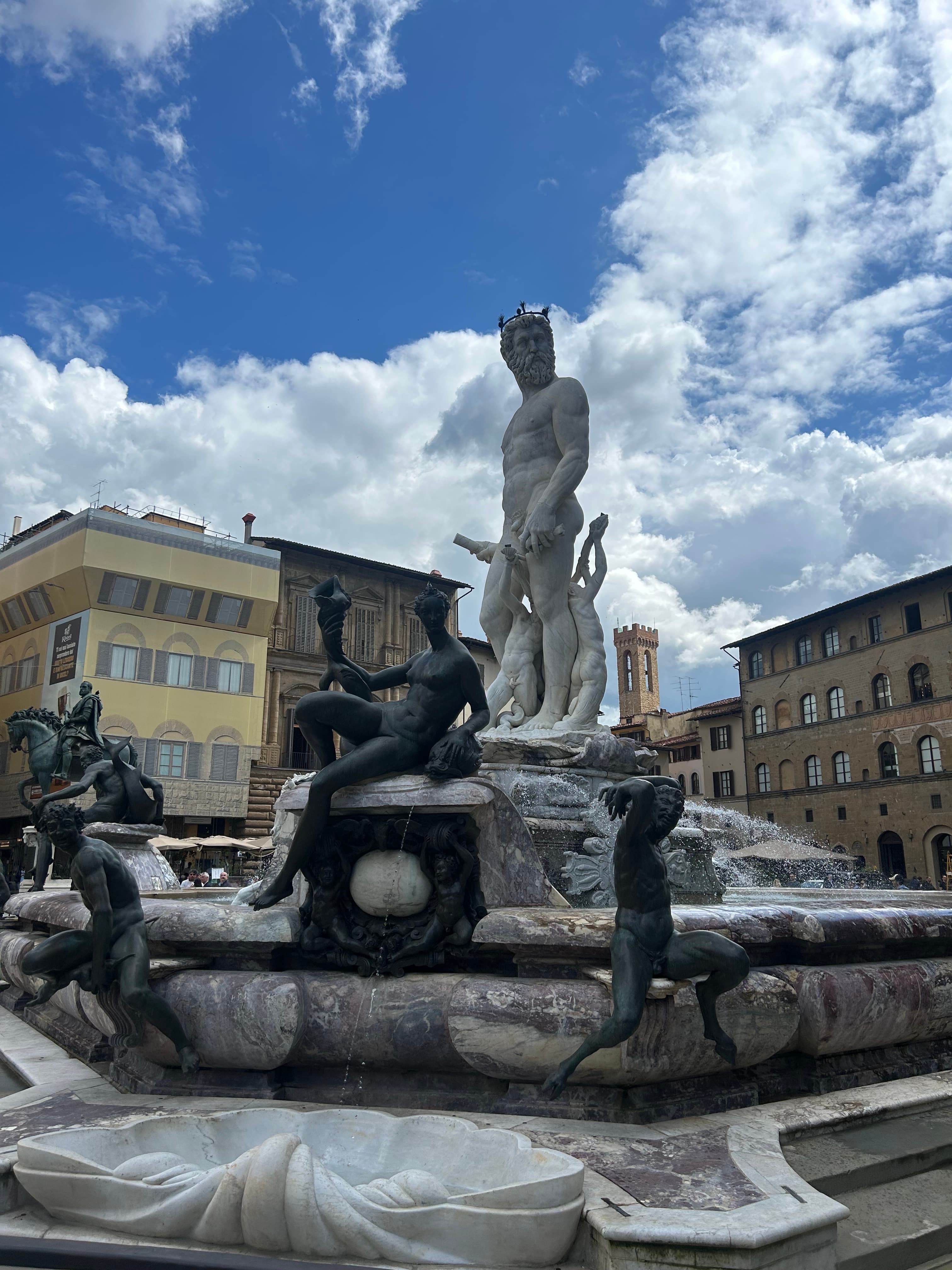 A decorative fountain featuring statues, set against a backdrop of elegant buildings.