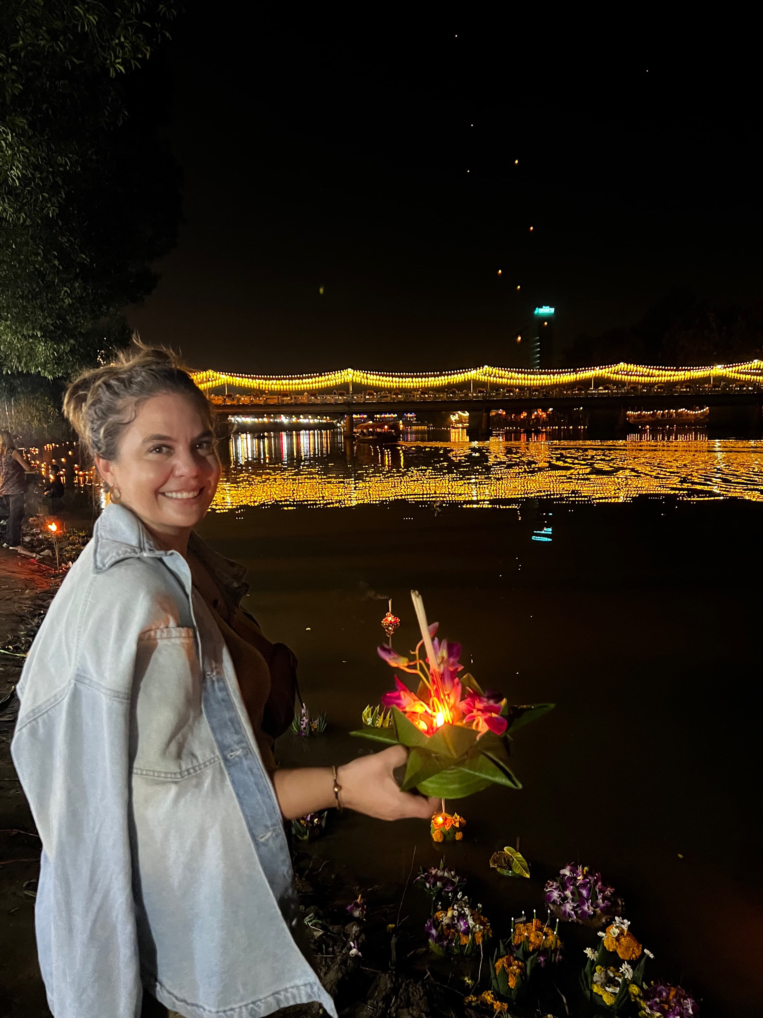Advisor holding a candle in a folded banana leaf at night with a bridge lit up in the distance