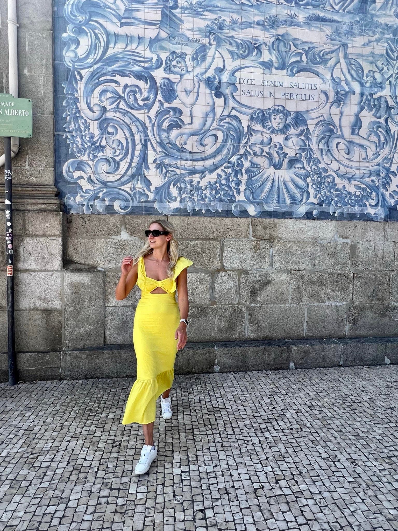 A person in a yellow dress standing in front of a blue tiled wall on the street