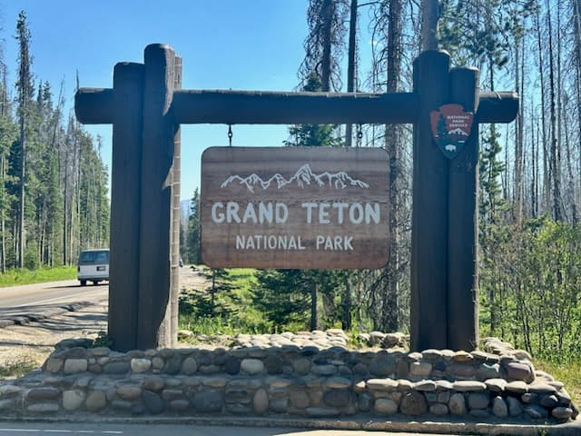 View of a wooden sign for Grand Teton National Park under sunny skies