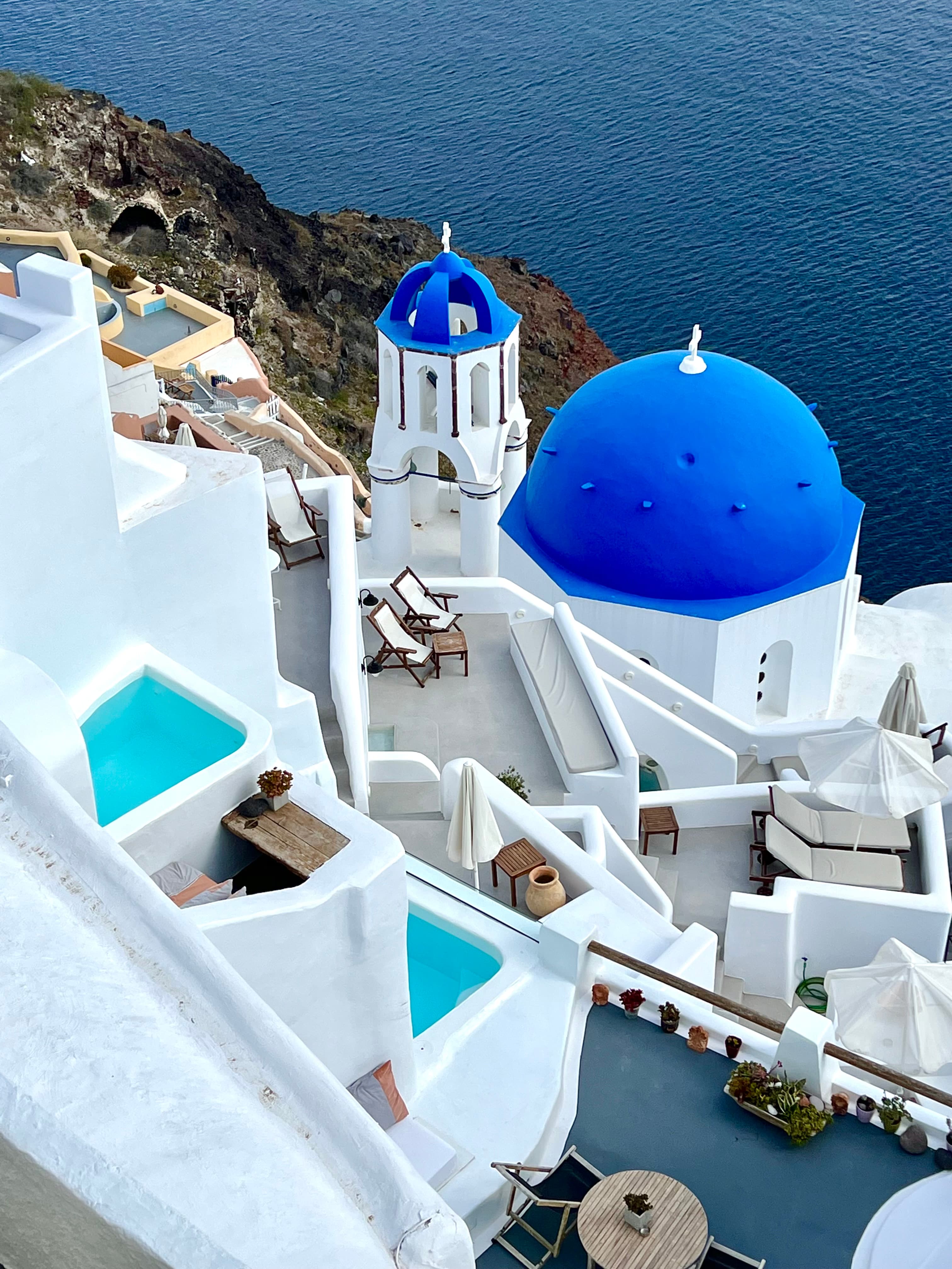 Overhead view of white buildings with blue rooftops by the sea in Santorini