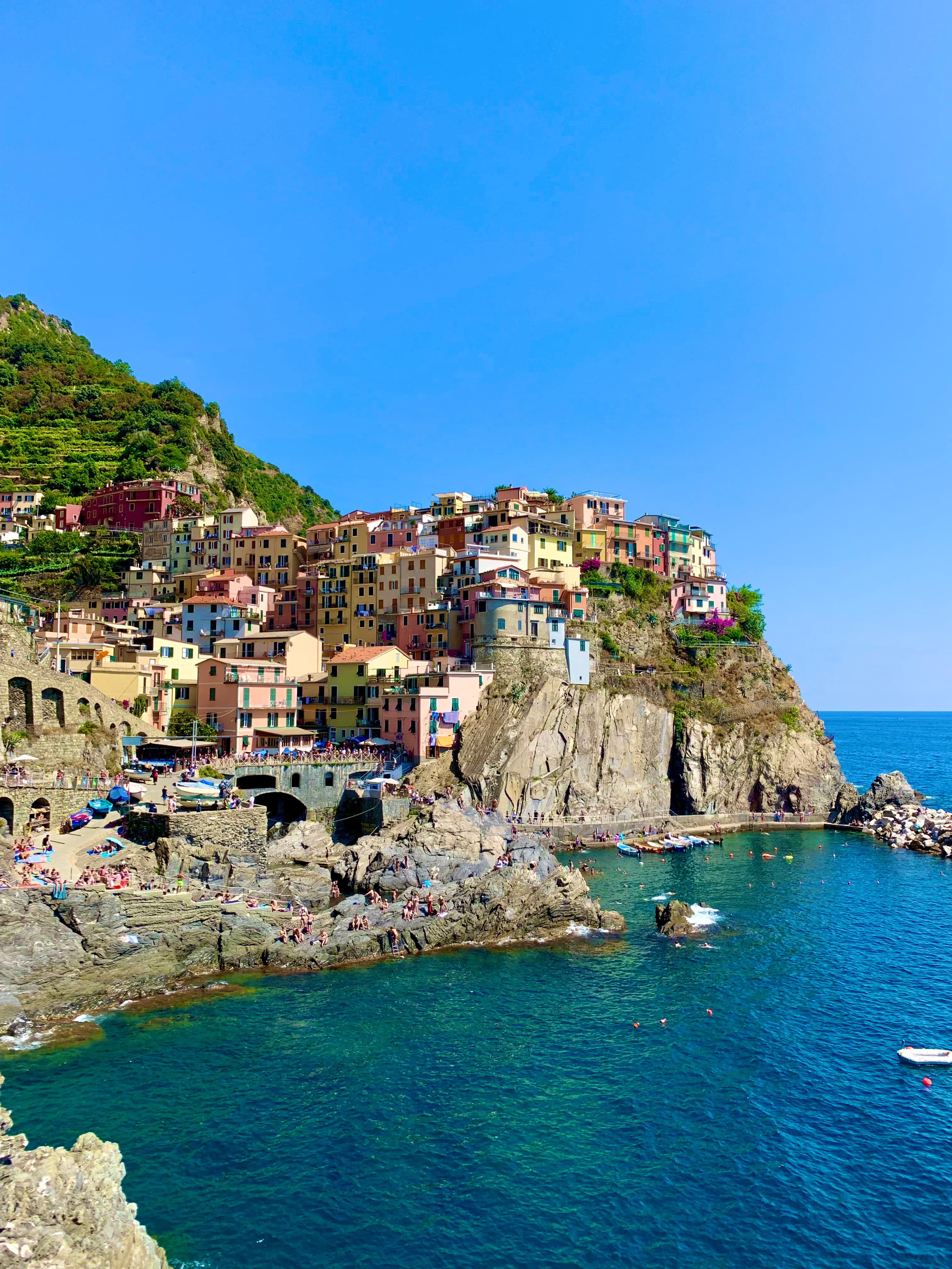 View of a buildings in small town perched on a cliffside overlooking a clear blue sea on a sunny day