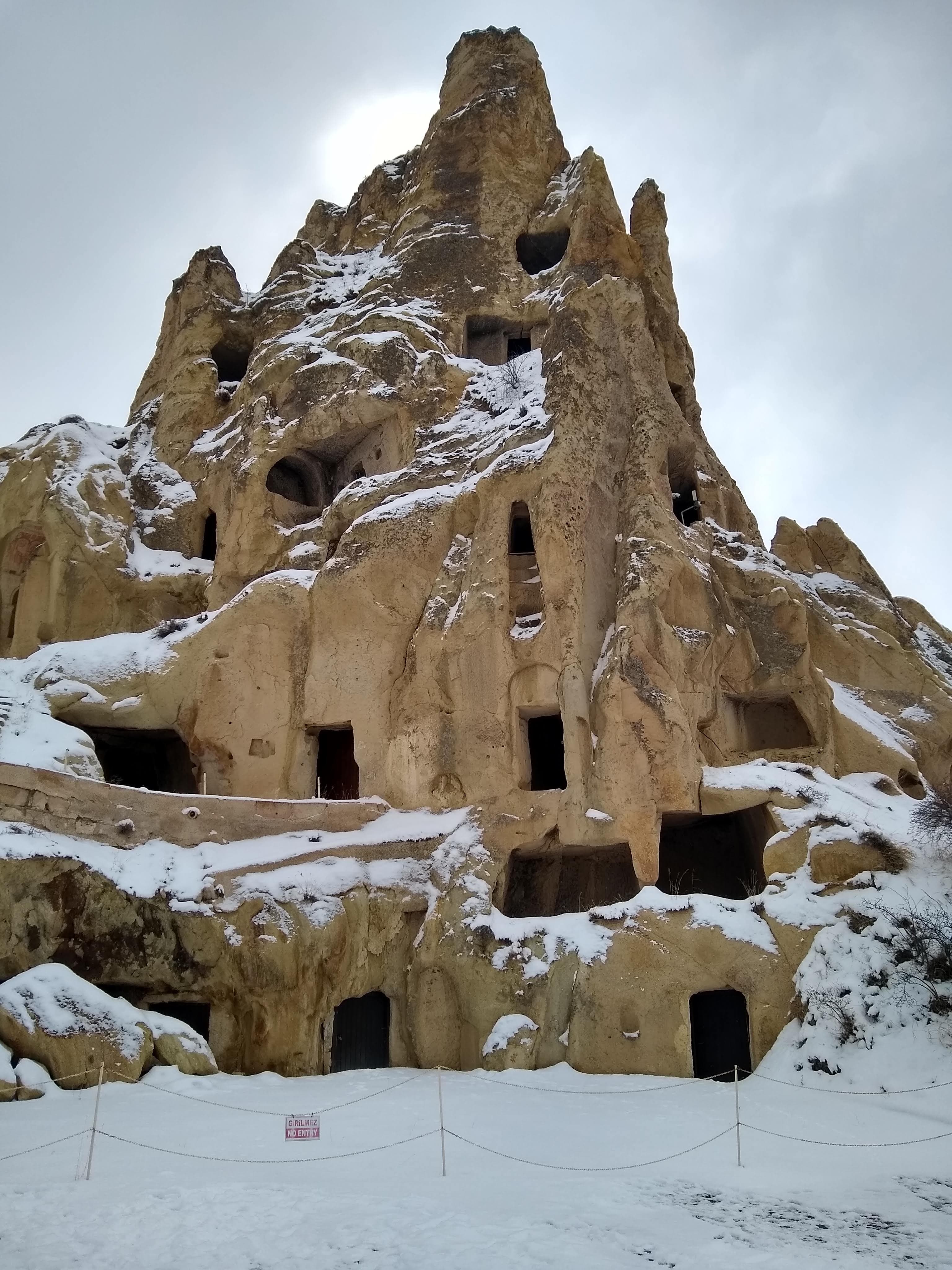 View of rectangular openings in the face of a rock formation covered with snow under cloudy skies
