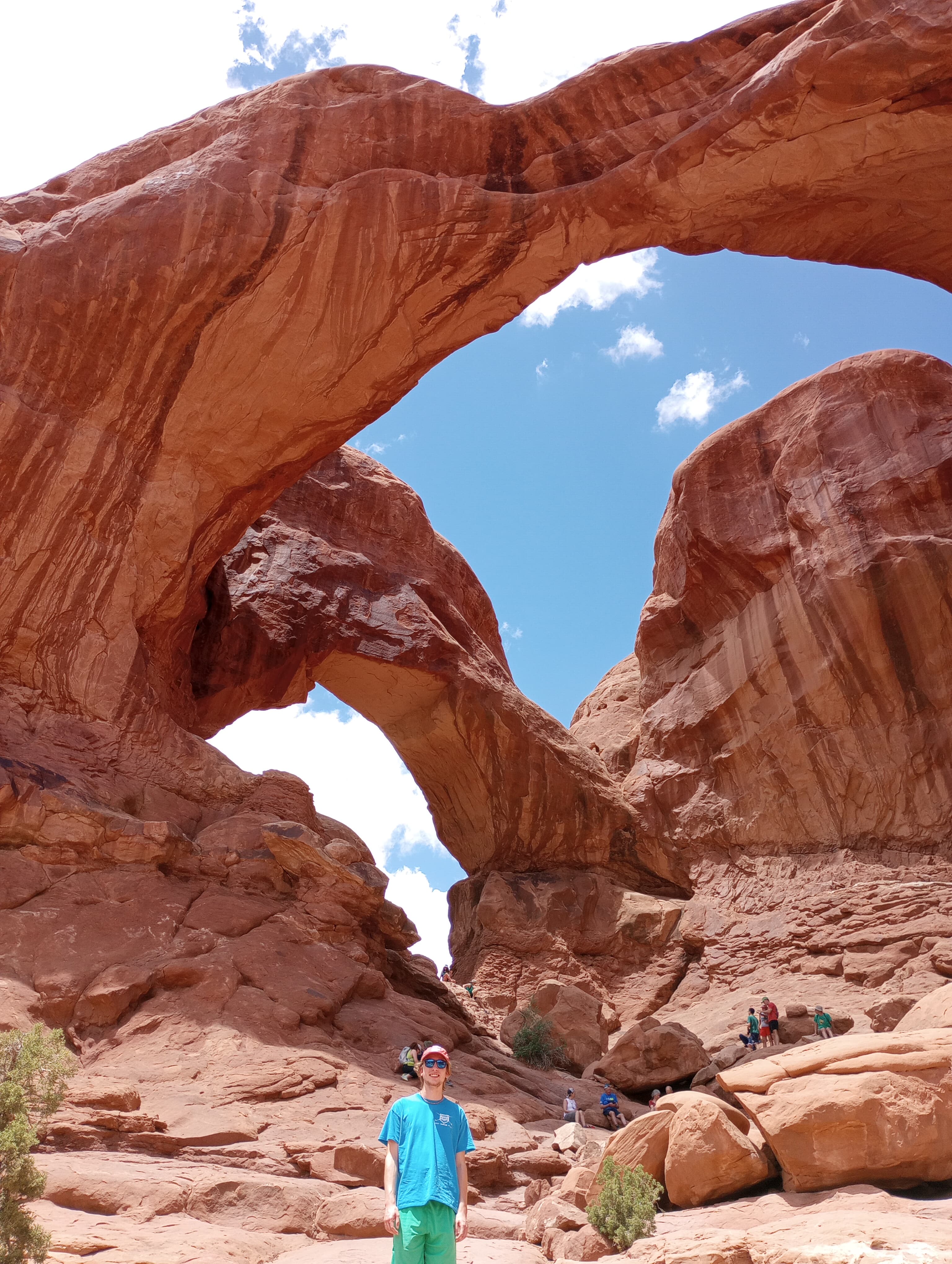 View of advisor standing below a large curved red rock formation on a sunny day