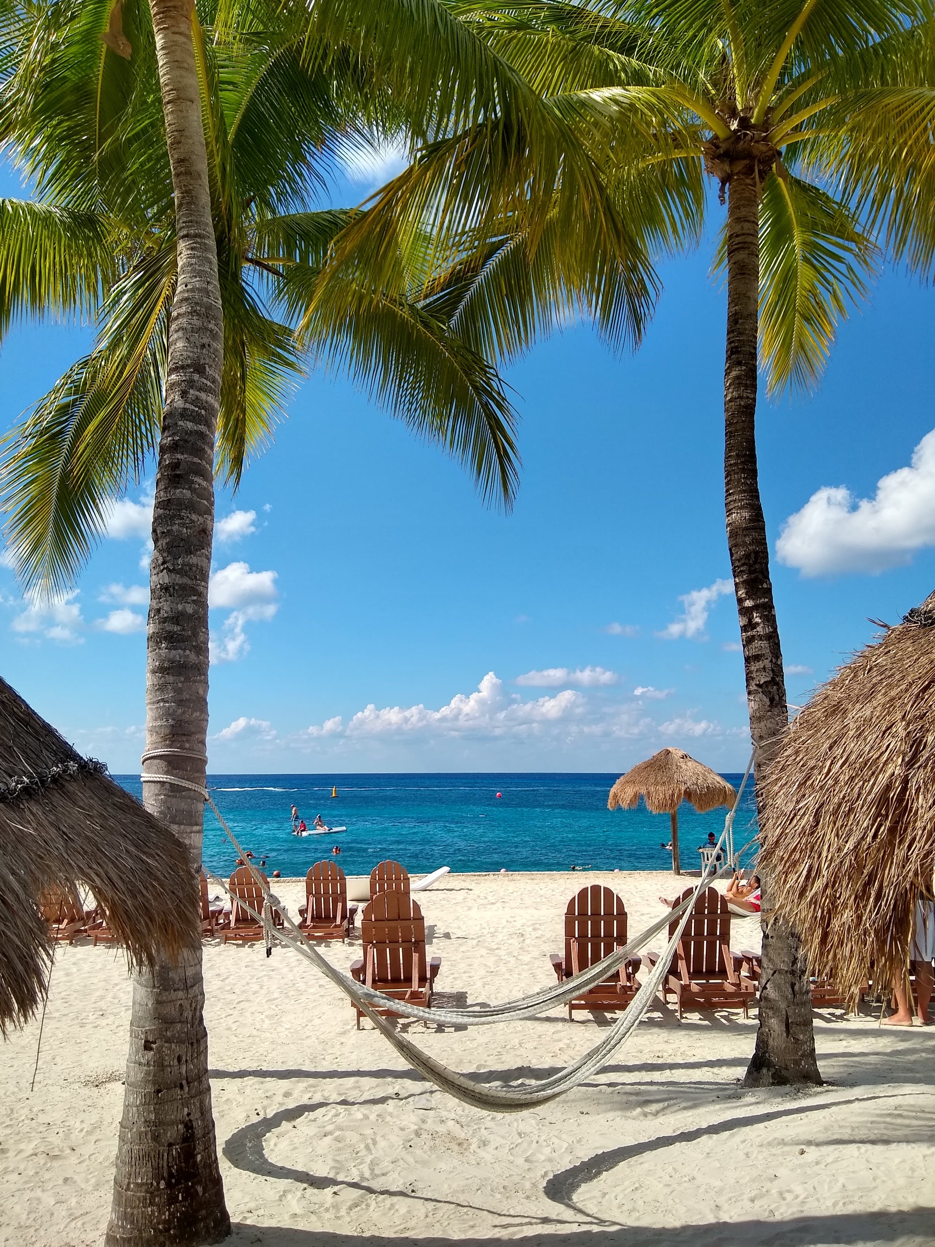 View of a beautiful white sand beach with chairs and a hammock between two palm trees