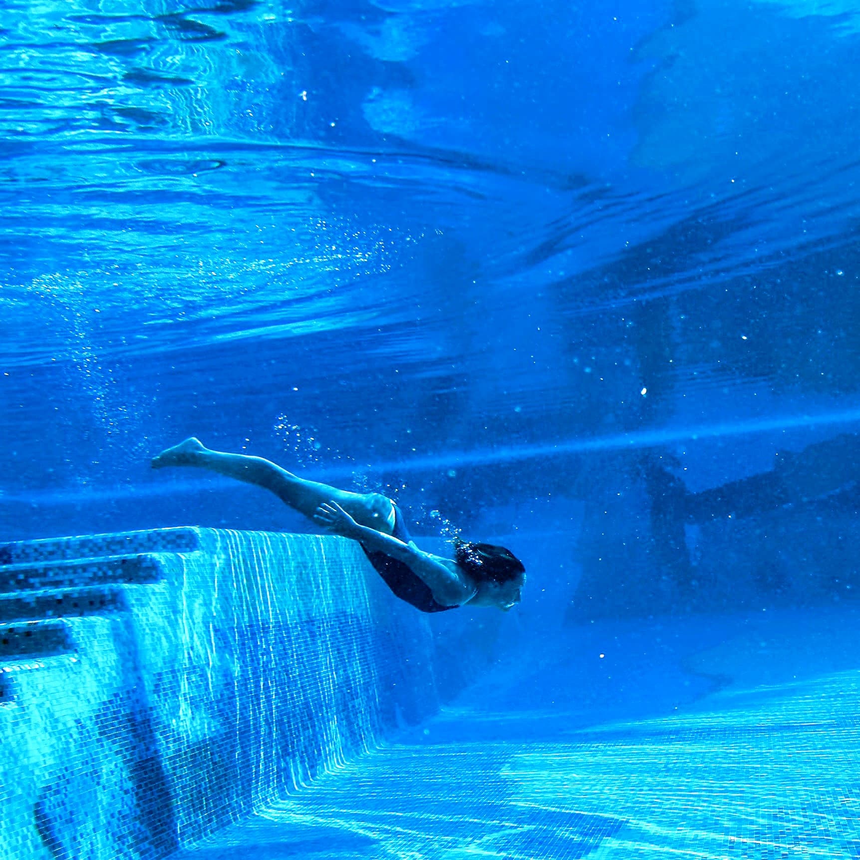 An underwater picture of a person swimming away from steps in blue water.
