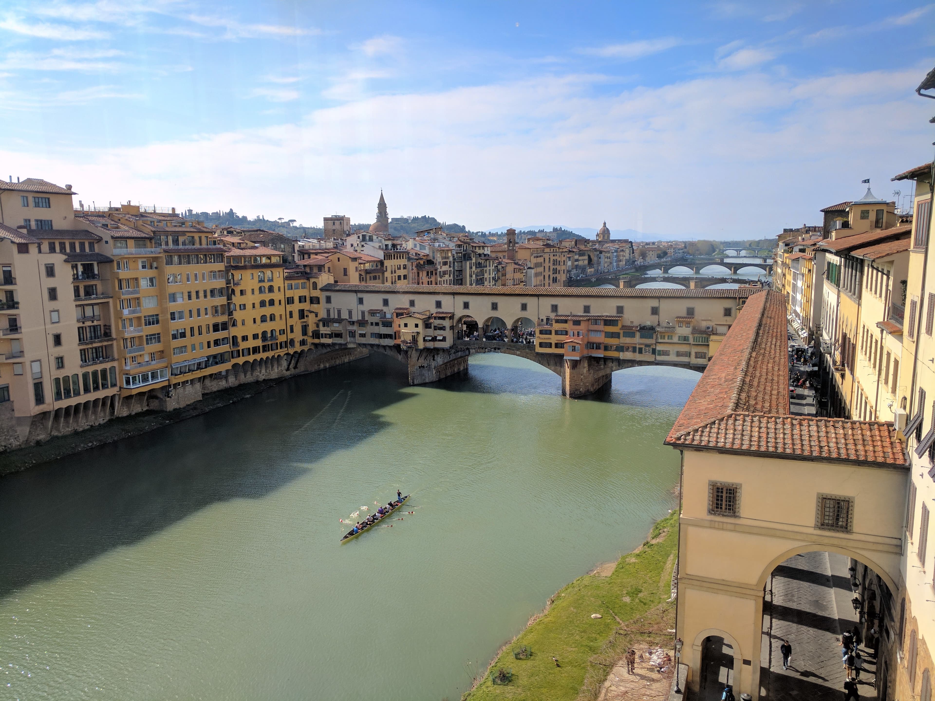 A view of a large river with a bridge and buildings on either side on a partly cloudy day.