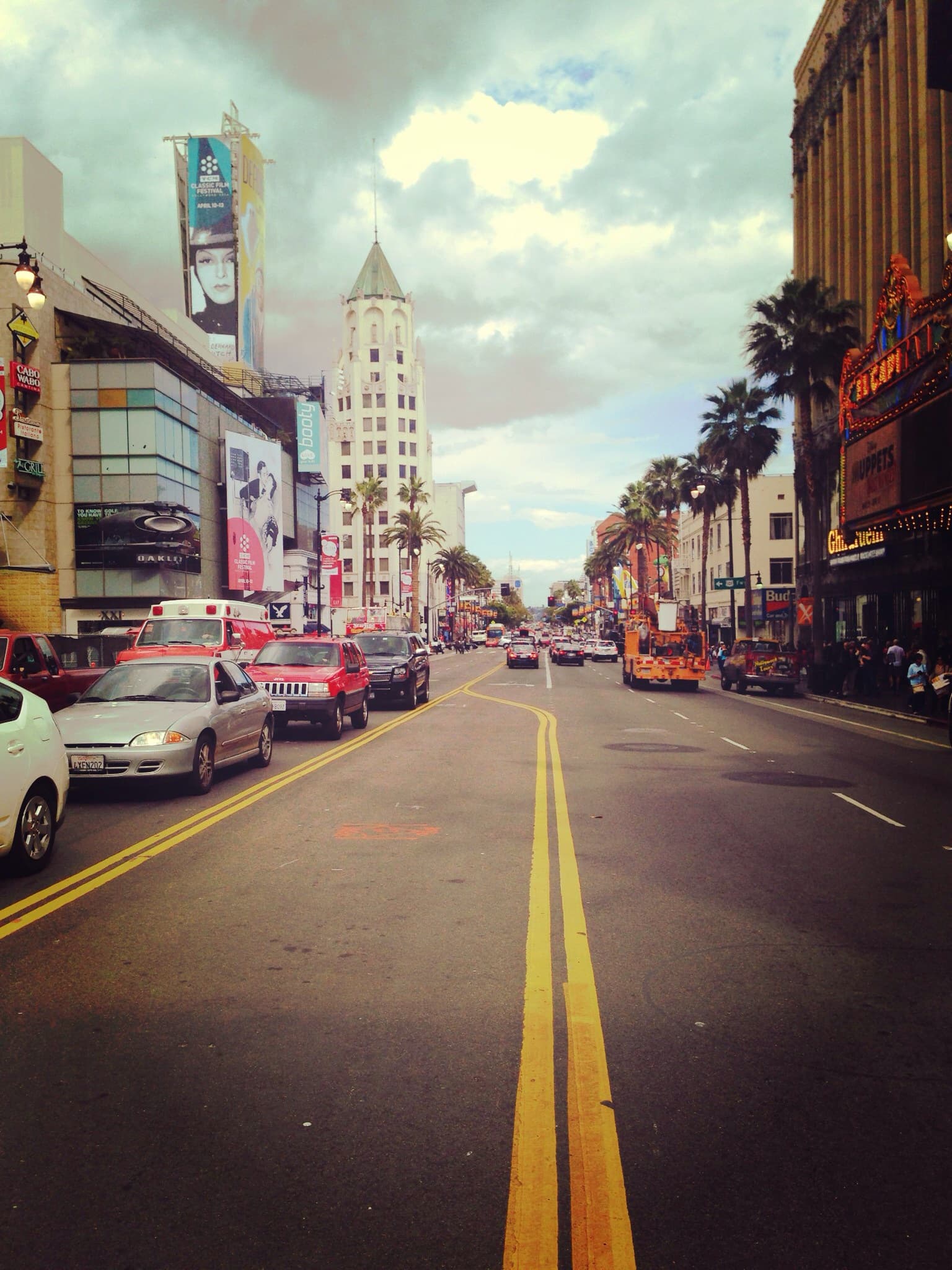 View of a city street with cars and palm trees to either side on a cloudy day