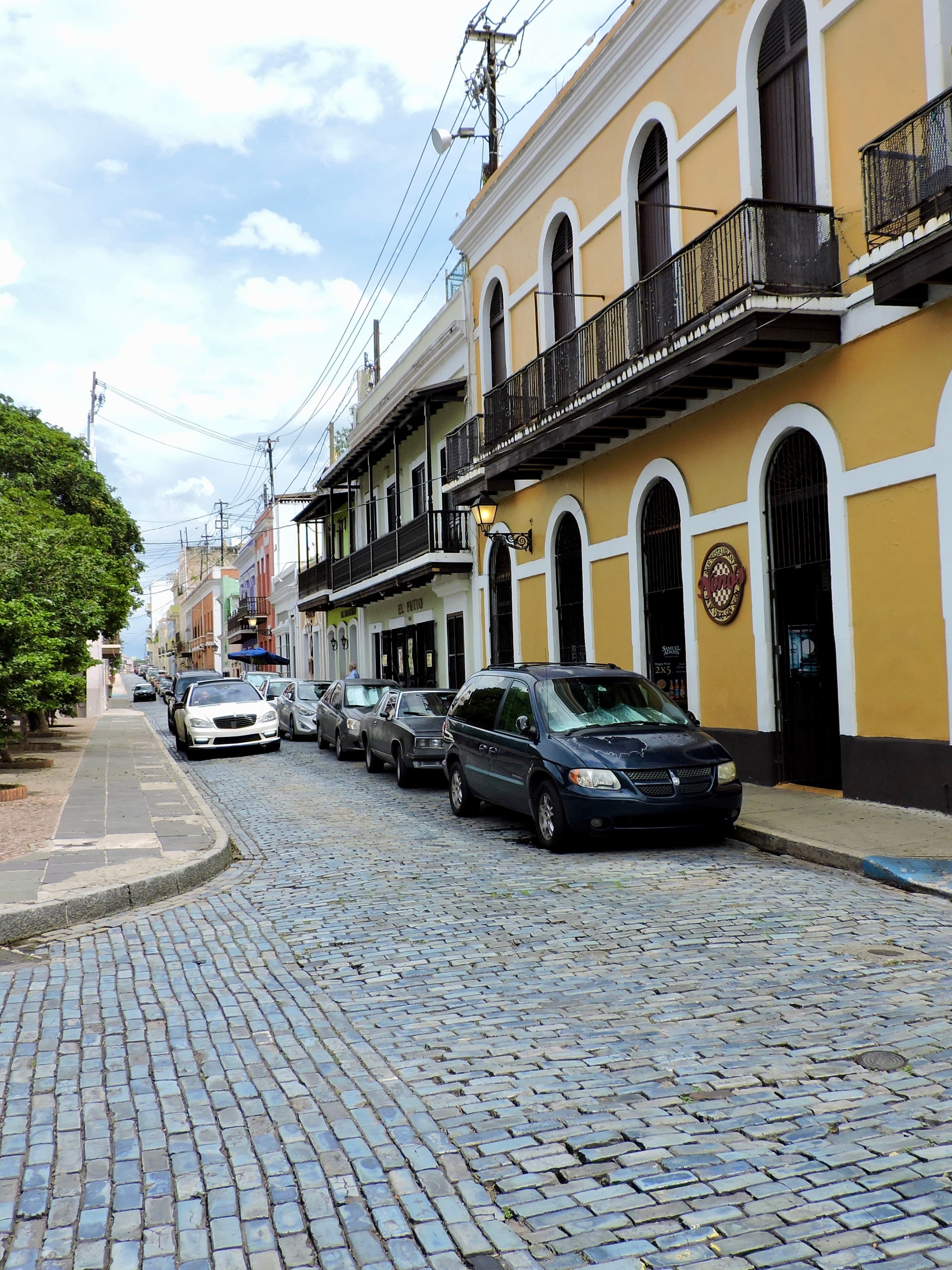 View of a cobblestone street with cars parked to one side in front of a yellow building