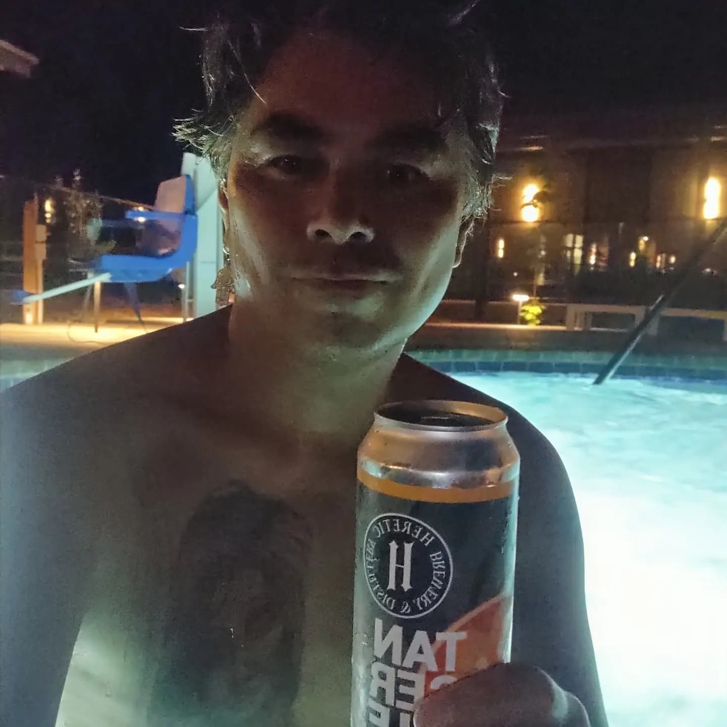 Advisor taking a selfie in a pool at night holding a can of beer