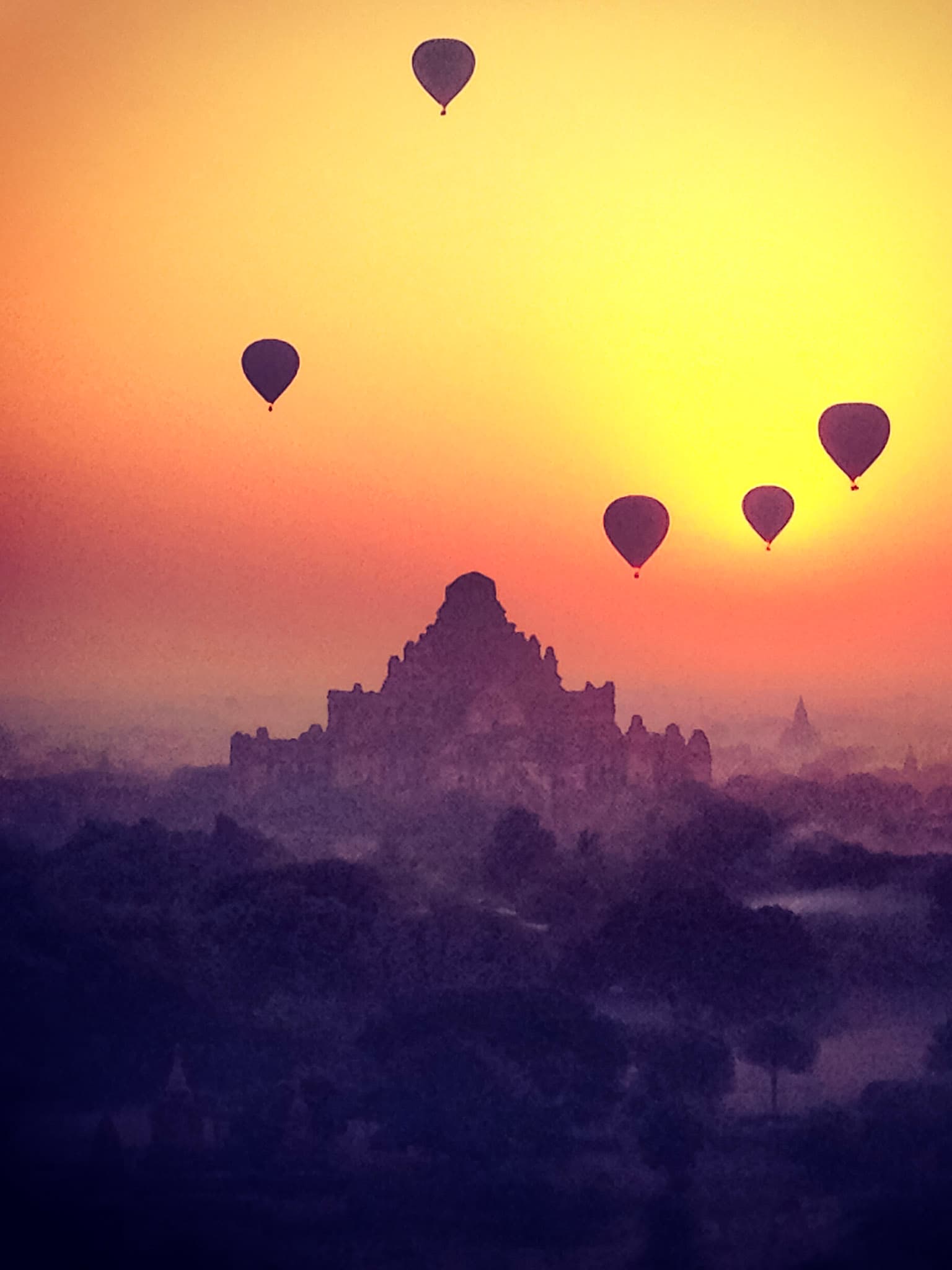 Beautiful sunset view of five hot air balloons flying over a mountain in silhouette against a yellow and orange sky
