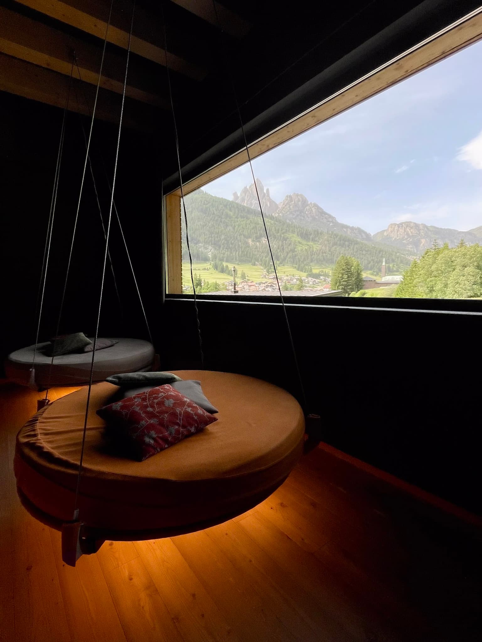 Interior view of a room with a hanging chair and pillows overlooking a green valley on a sunny day