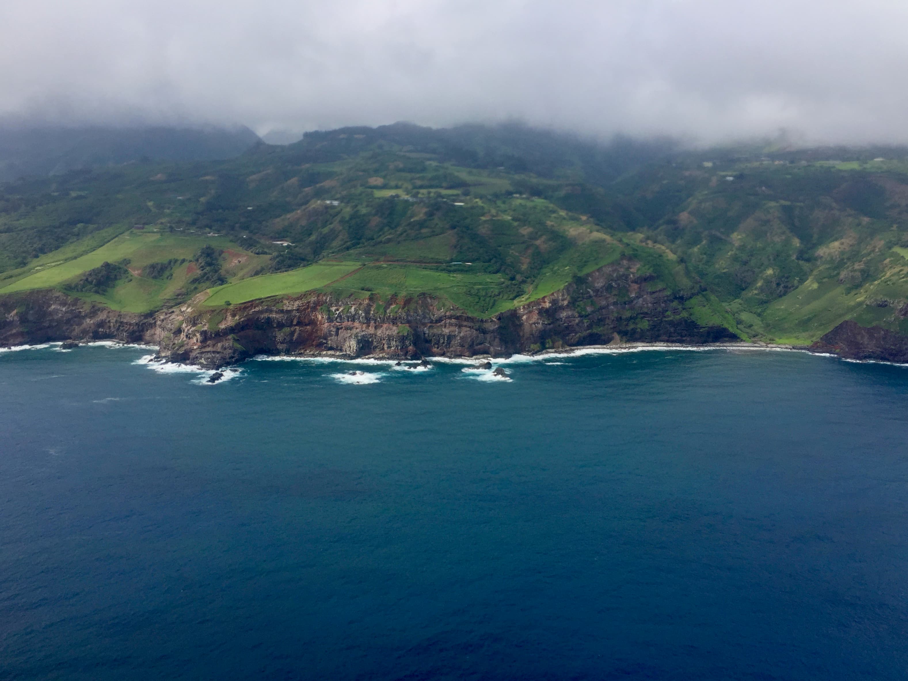 An aerial view of the ocean and the coastline with lush, green mountains with a layer of fog overtop.