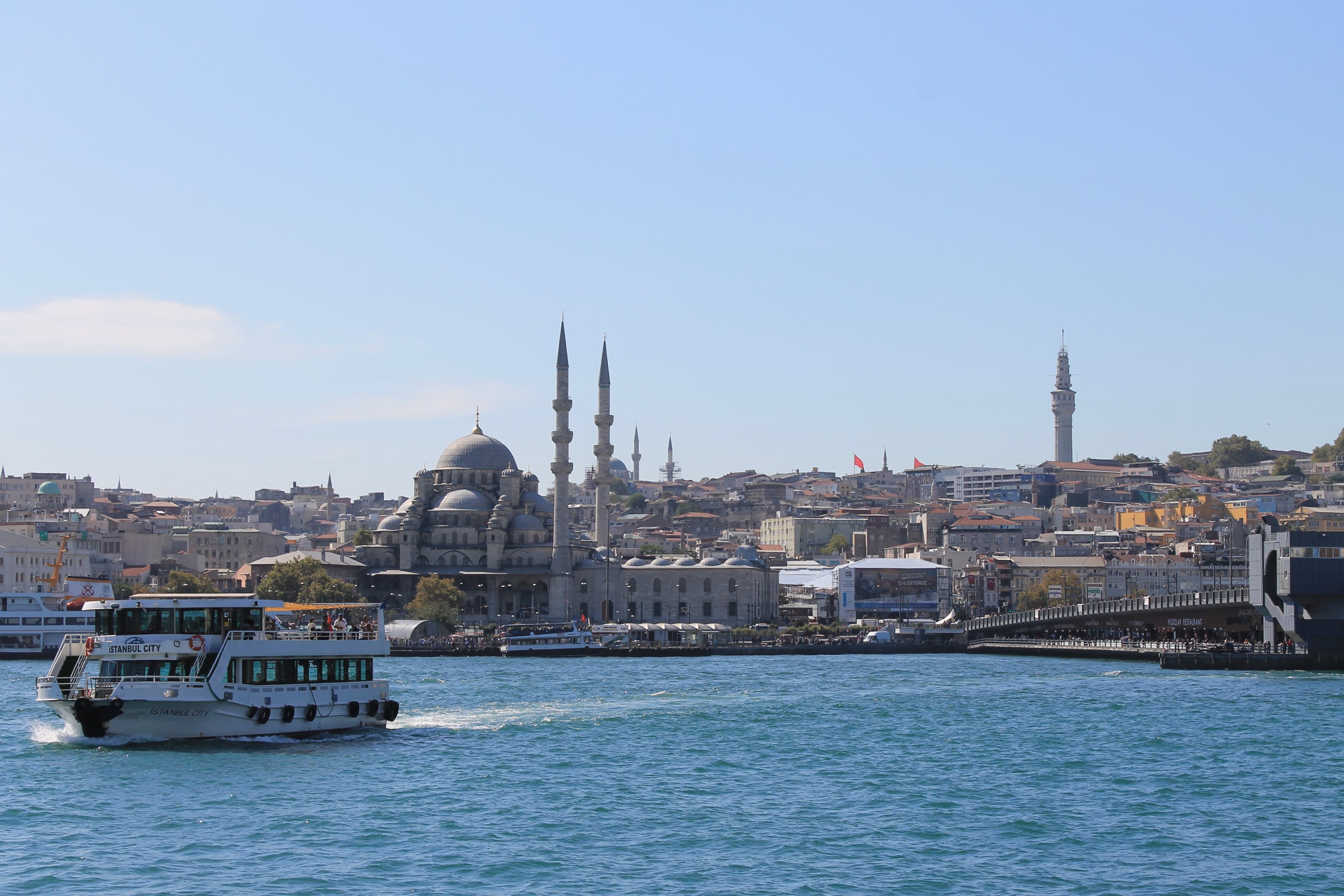 A view from the ocean looking at a boat cruising towards a historical city on the coastline during the day.