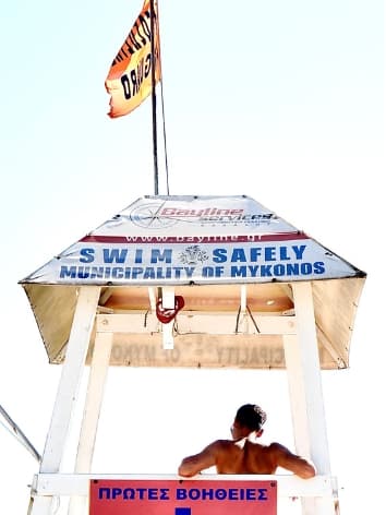 View from behind of advisor sitting on a life guard’s chair in Mykonos on a sunny day