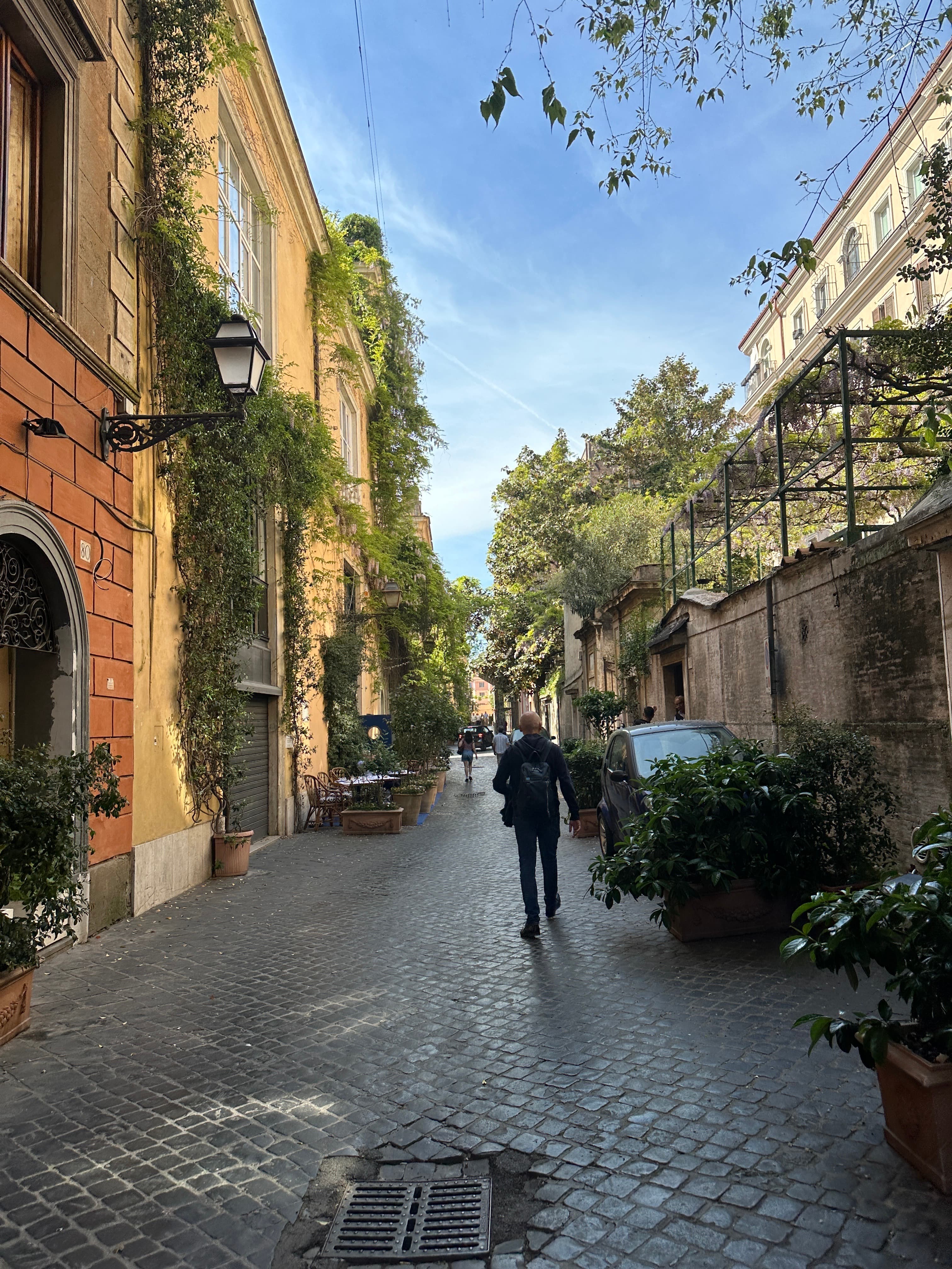 View of a person walking along an empty cobblestone street lined by yellow buildings on a sunny day