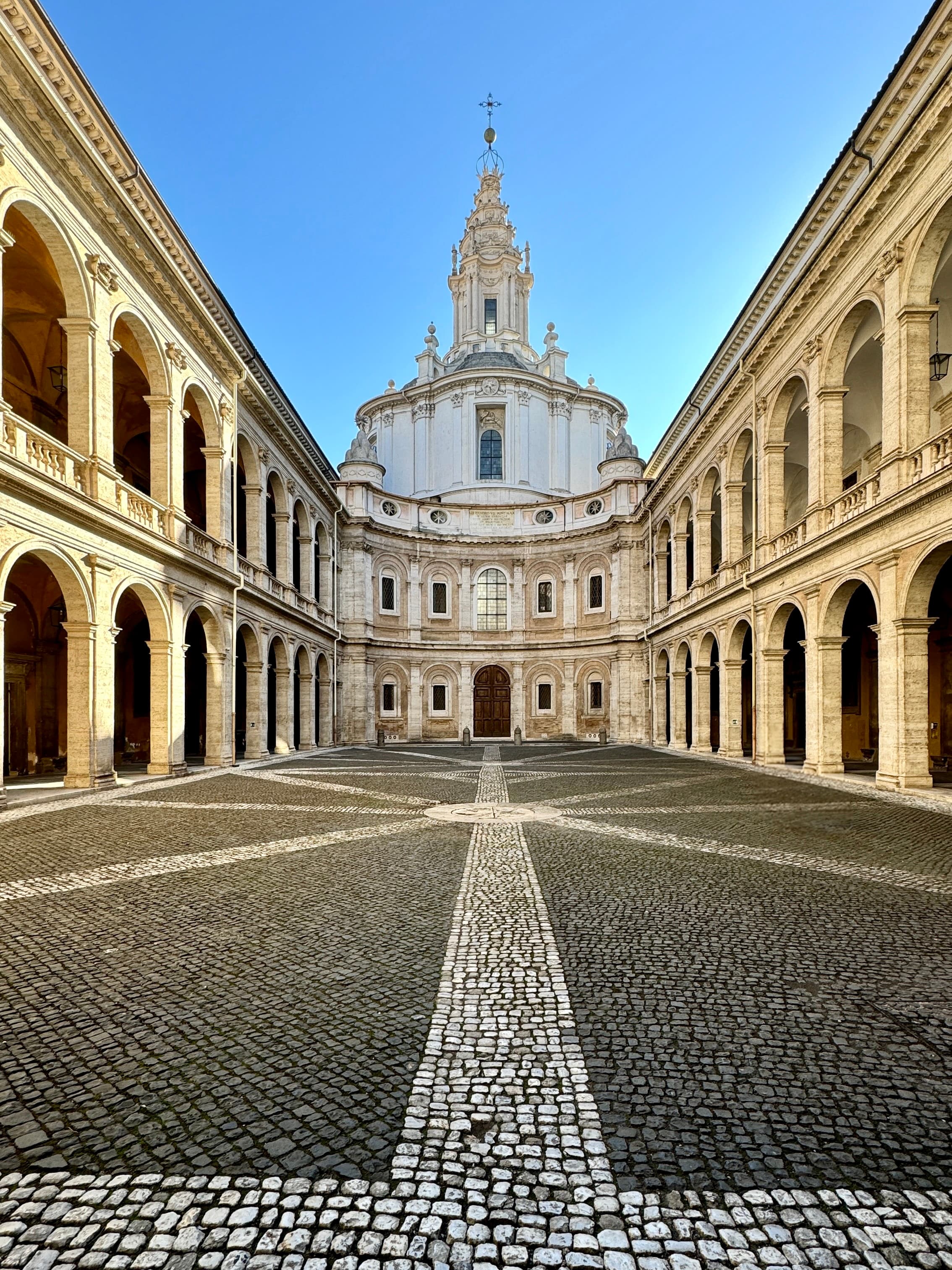 View of an empty plaza lined with columns on both sides and a beautiful cathedral at the back
