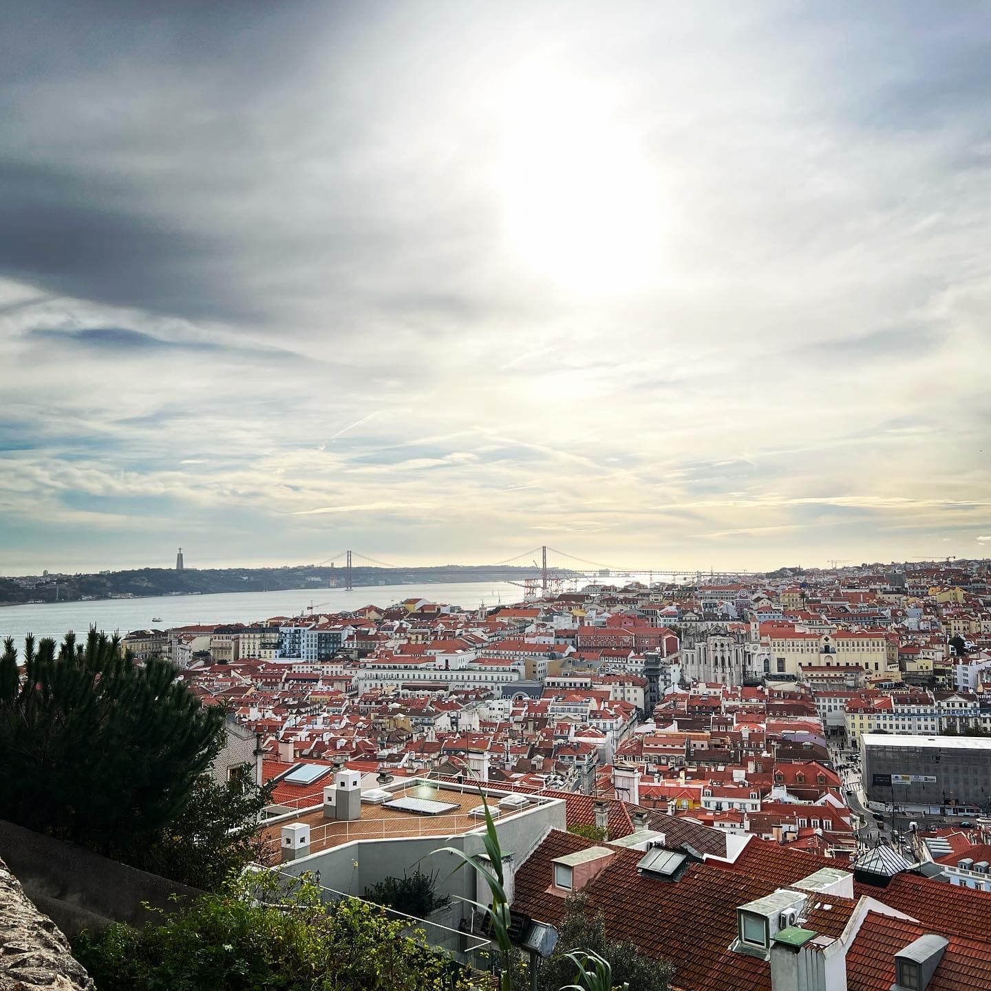 Panoramic view of a city with orange rooftops under sunny skies and a river in the distance