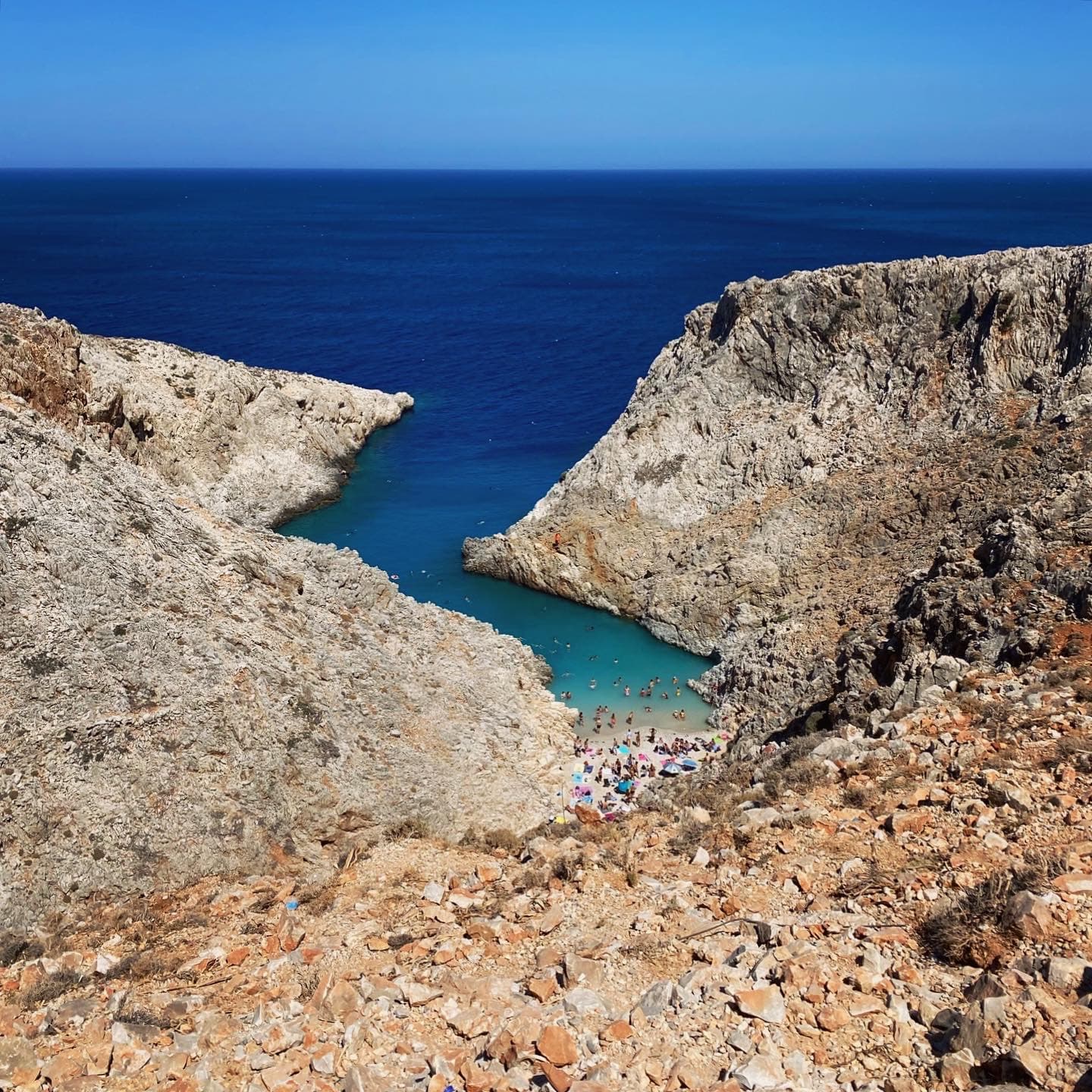 Aerial view of cliffs forming a canyon at the ocean’s edge and a small bay with sunbathers